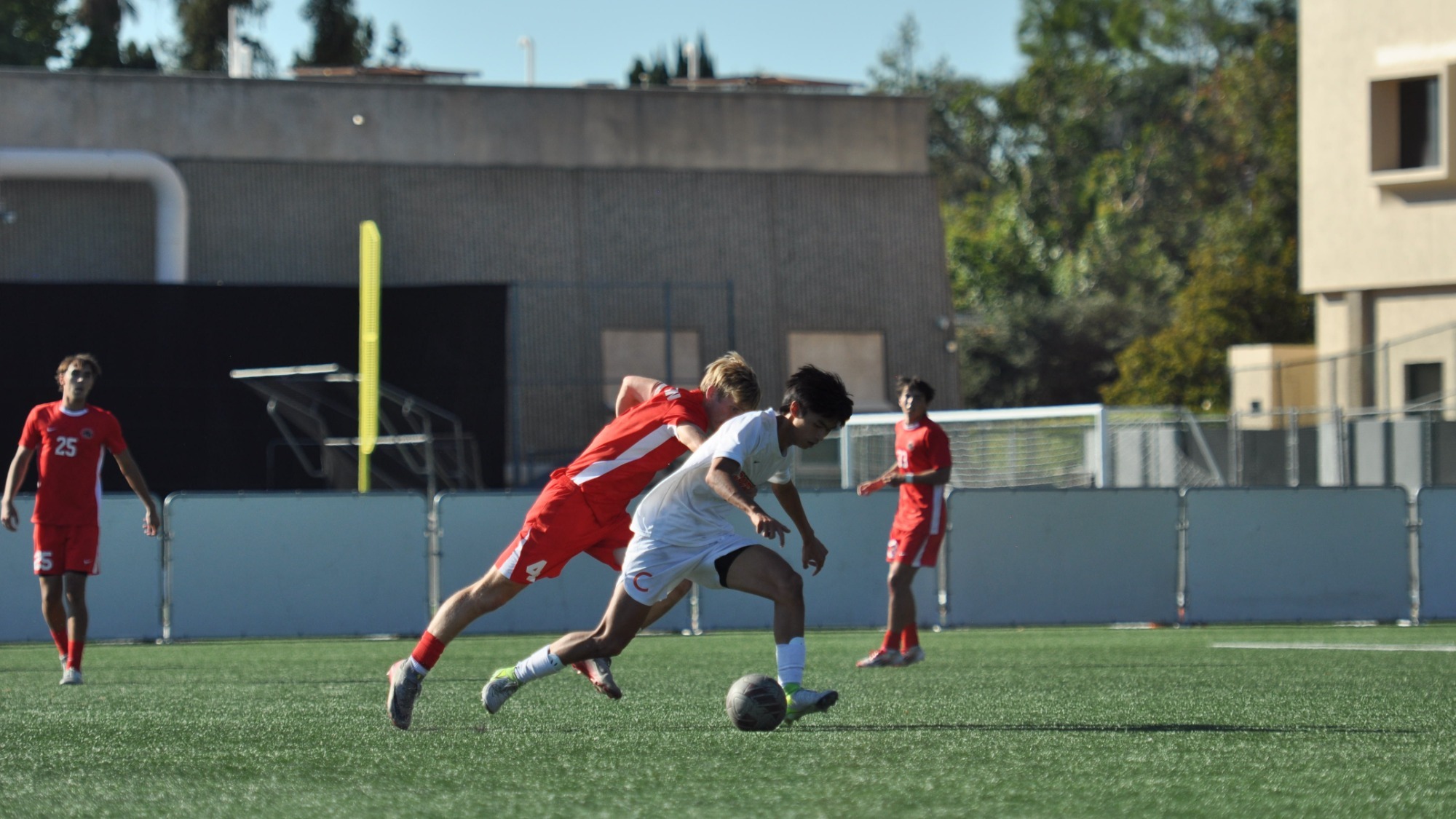 Matthew Luk, wearing white, lowers his center of gravity as he dribbles against a defender wearing red behind him. The defender reaches out, clearly beaten on the play. 
