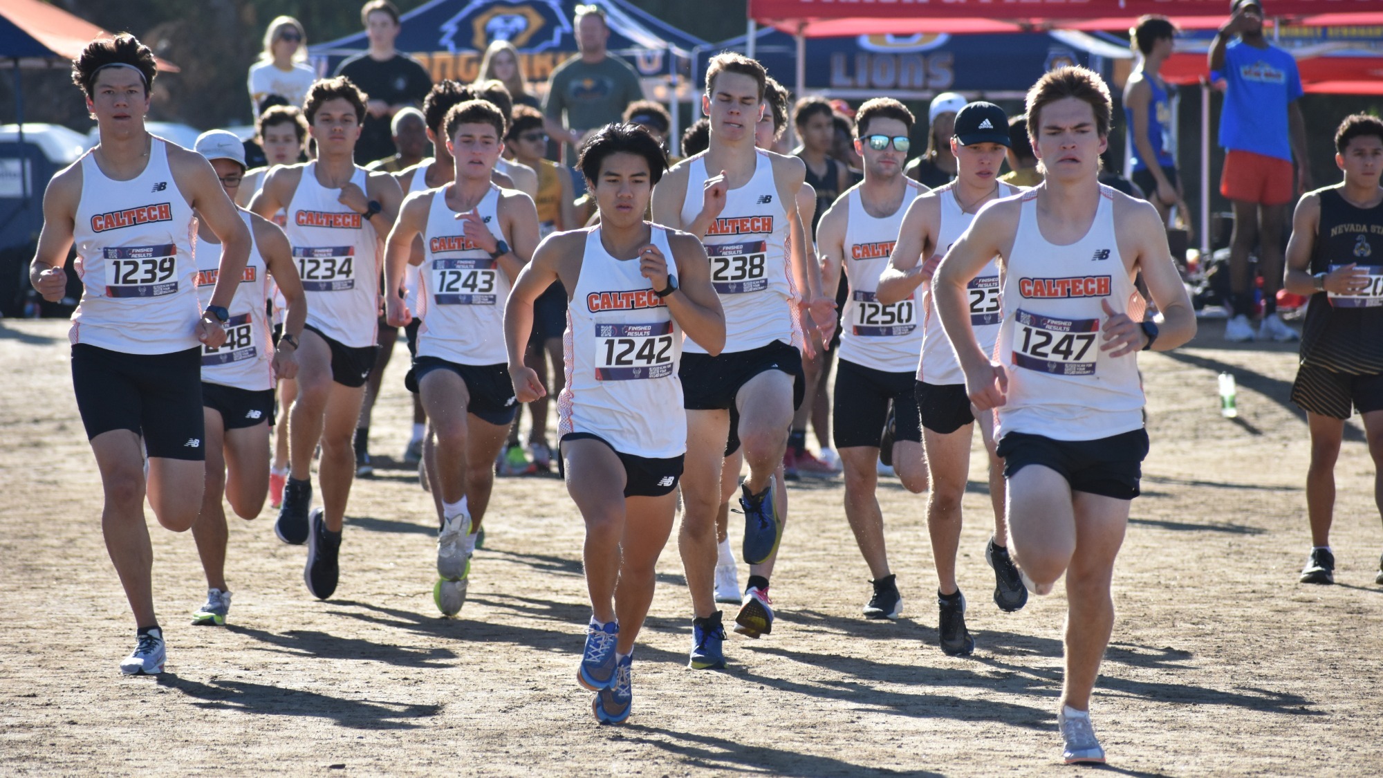 10 Caltech male runners, all wearing white tops and black shorts, run towards the camera as they warm up at the UCR Invitational. 