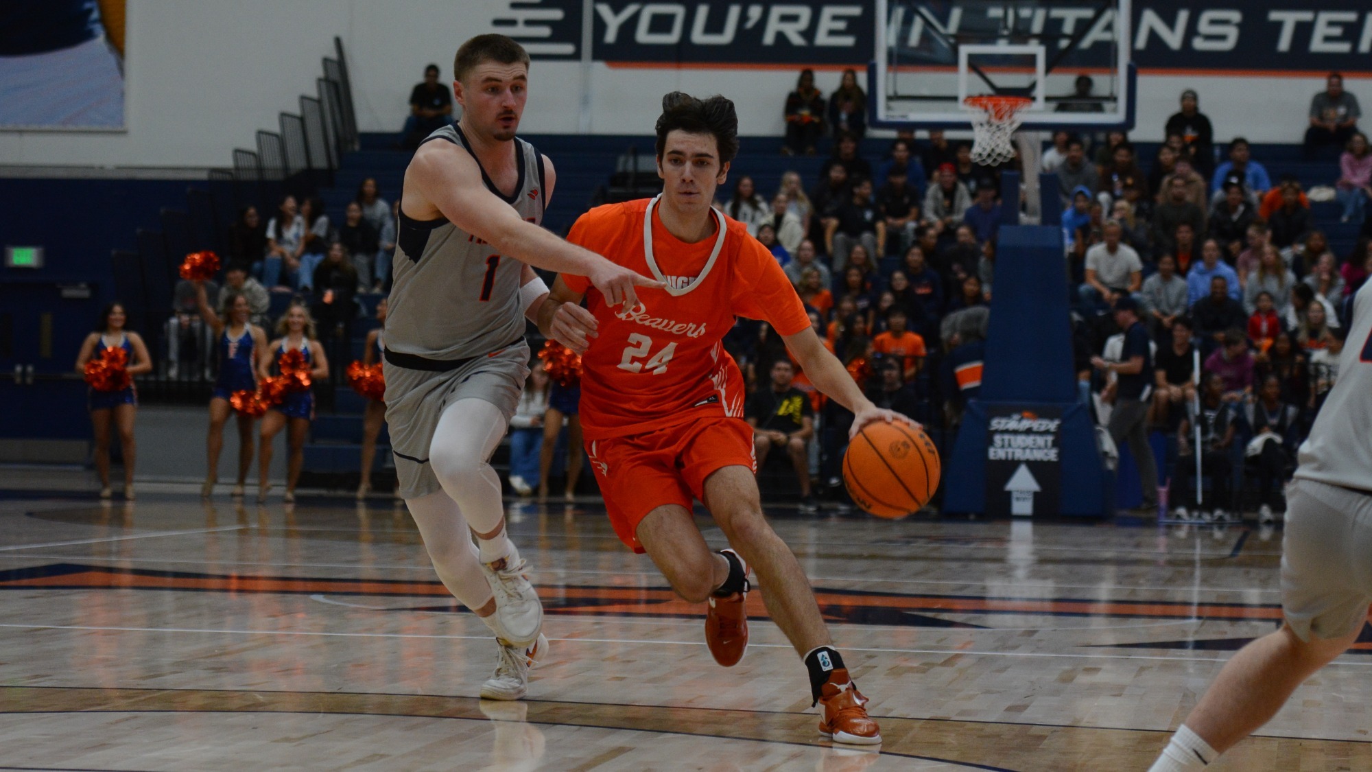 Dorian Glogovac drives towards the basket from the top of the key as viewed from under the basket. He holds the ball in his left hand while fighting off a defender with his right. 