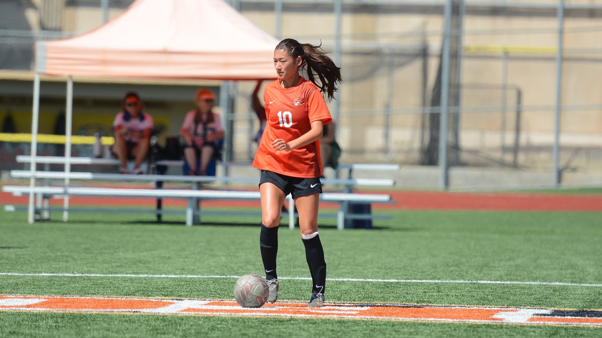 Wearing and orange #10 jersey and black shorts, Ellie Yamada calmly controls the ball with her right foot, assessing her next move. 