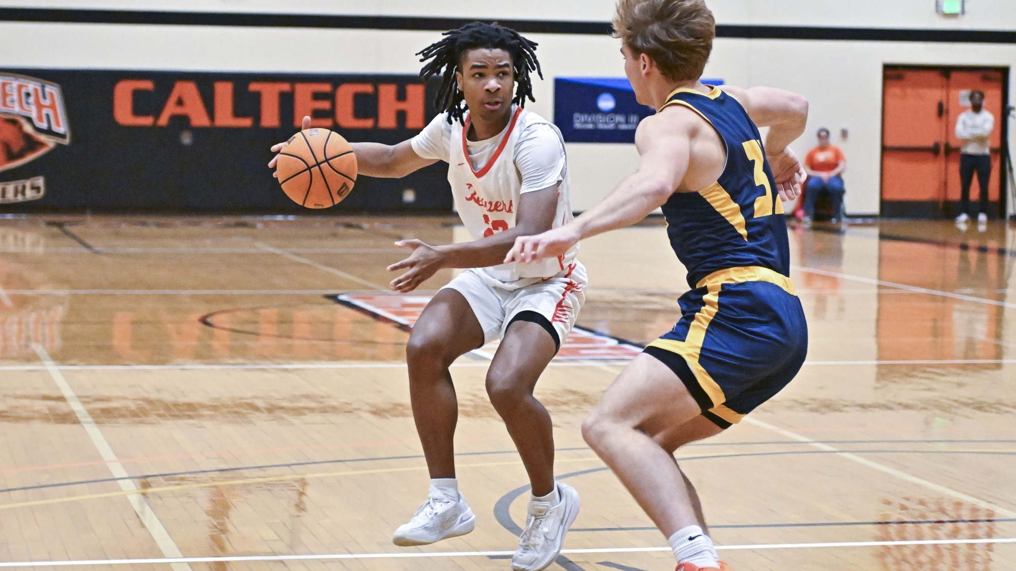 Chase Williamson controls the ball in his right hand as he steps back at the elbow against a UCSC defender. The defender wears a blue jersey with yellow trim. Williamson is in a white jersey with orange trim