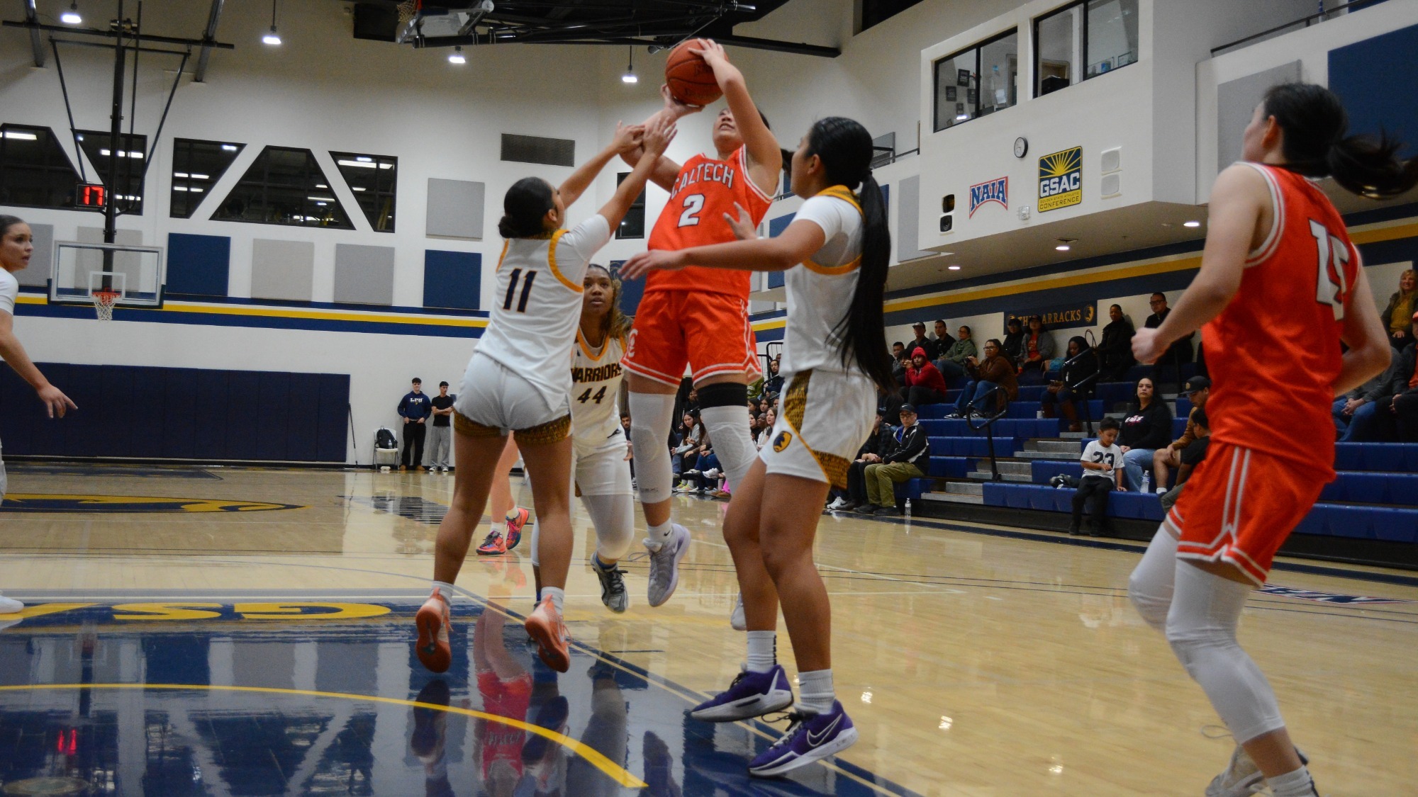 Kyra Phaychanpheng jumps with the ball in both hands above her head as she attempts a shot against two defenders who are both jumping late. 