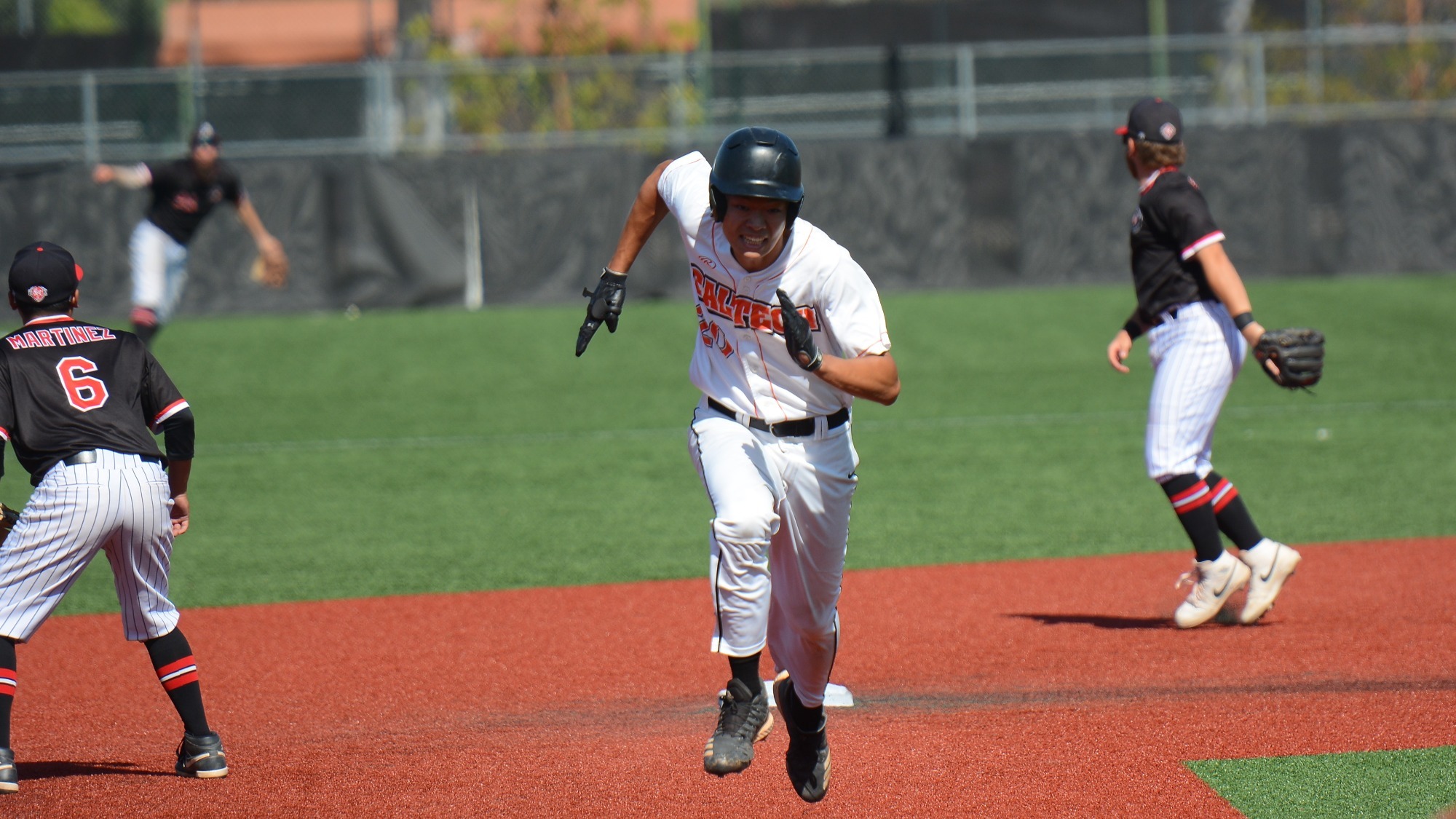 Mark Hu runs from second to third base, grimacing and wearing a white uniform. 