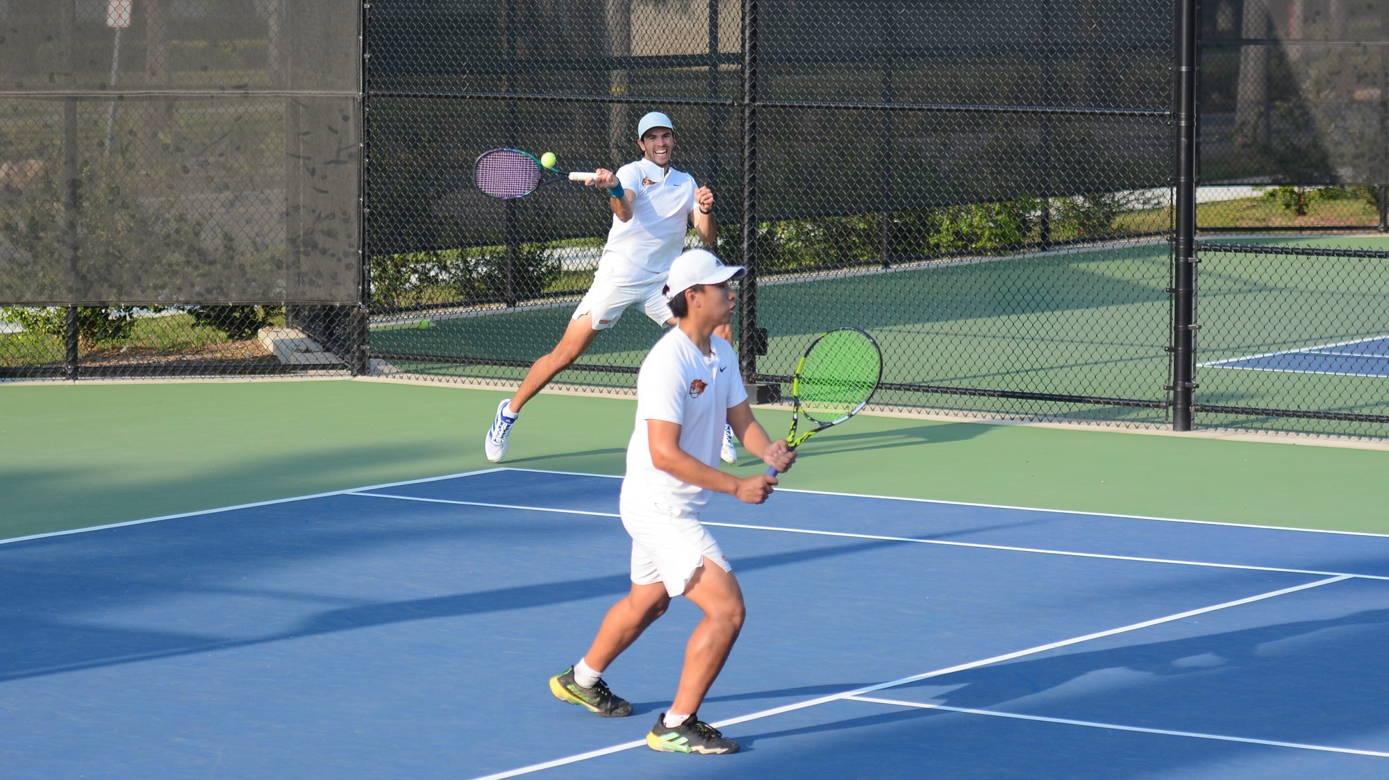 Eric He stands ready as doubles teammate Andrew Zabelo returns a ball with his forehand near the back corner.