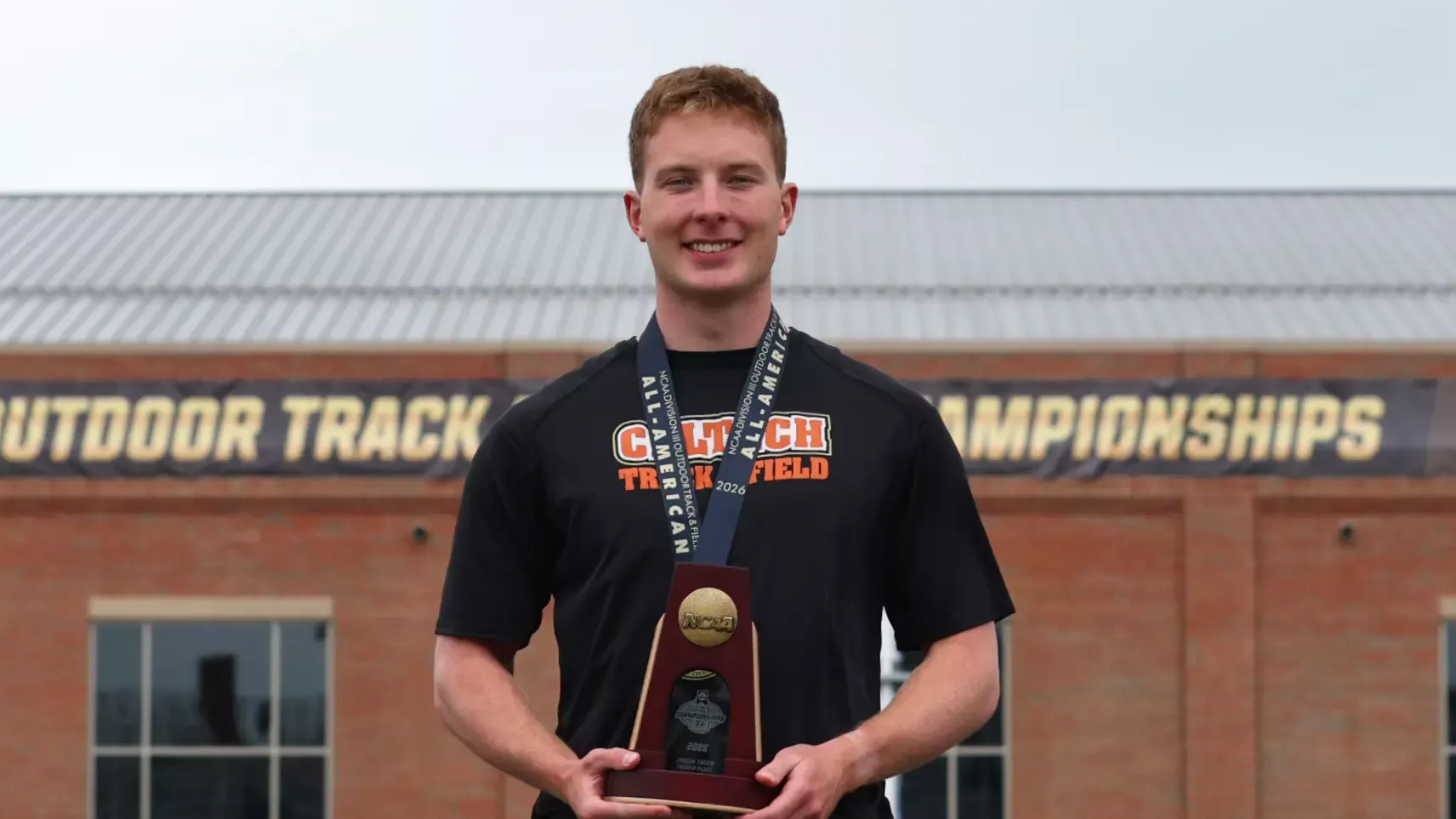 Luke Lamitina stands on the podium, holding his All-American medal and holding his NCAA Championships Fourth Place Javelin Throw trophy