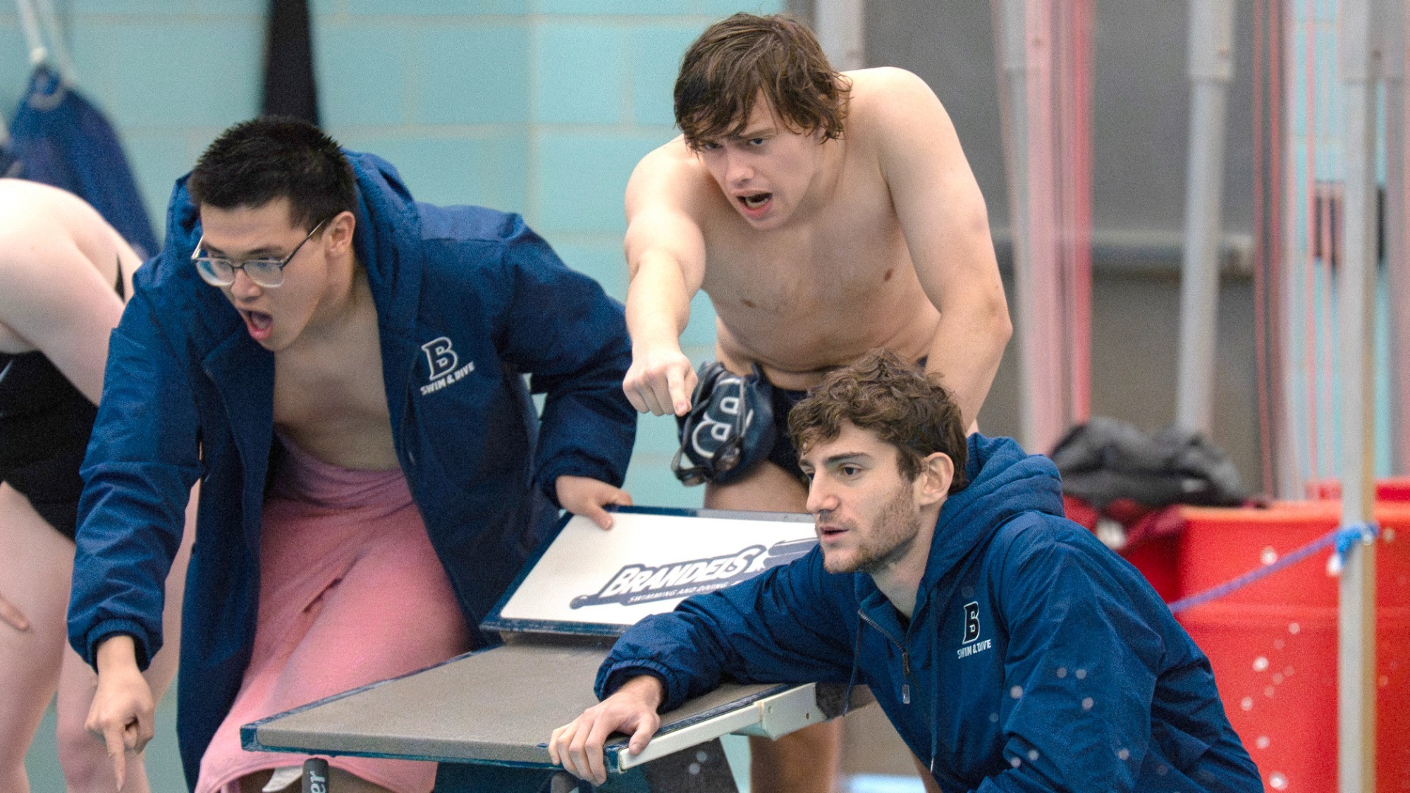 Three Brandeis swimmers encourage their teammates from the deck