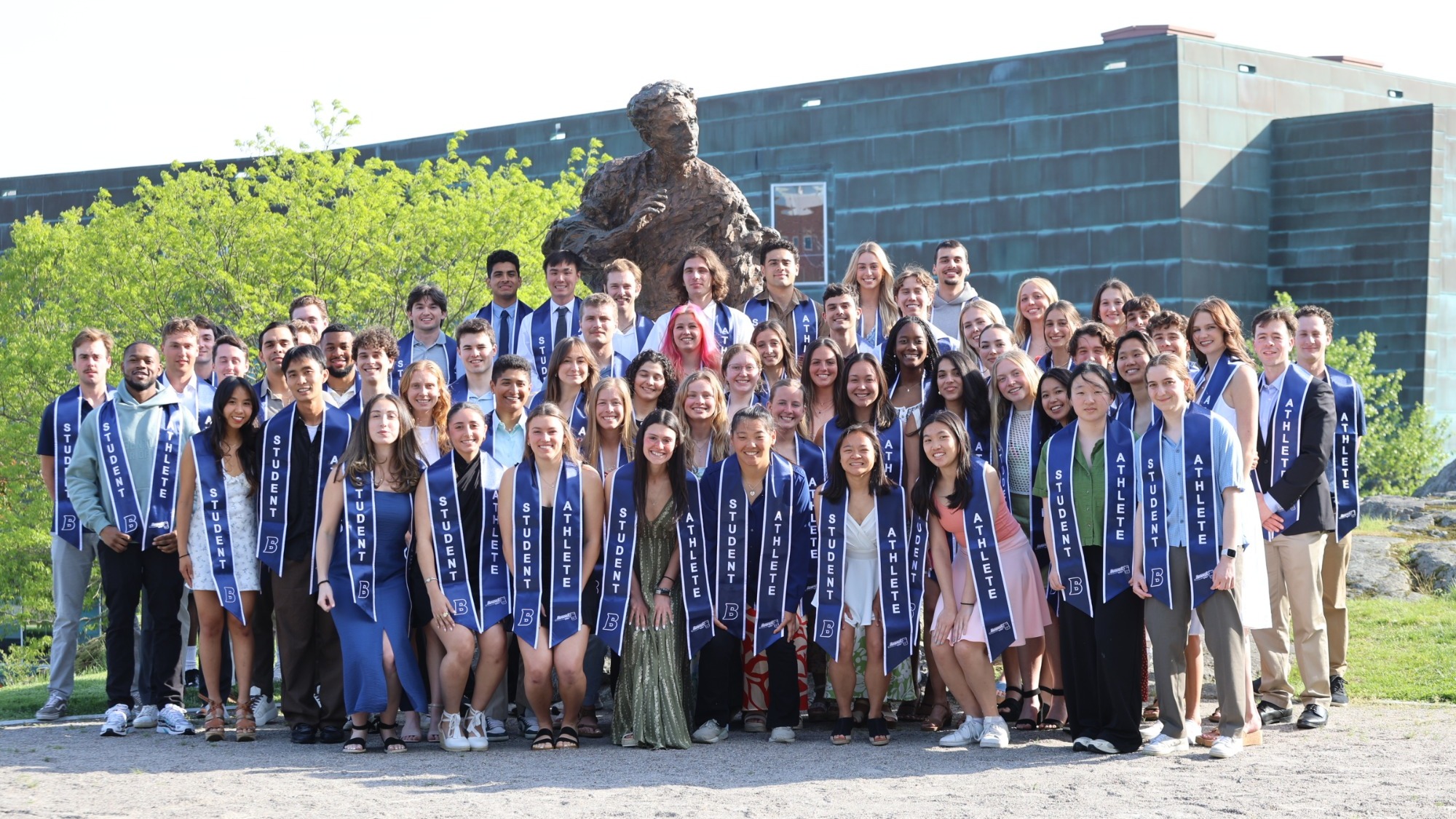 Members of the Class of 2025 posing in front of the Louis Brandeis statue with the Shapiro Campus Center in the background