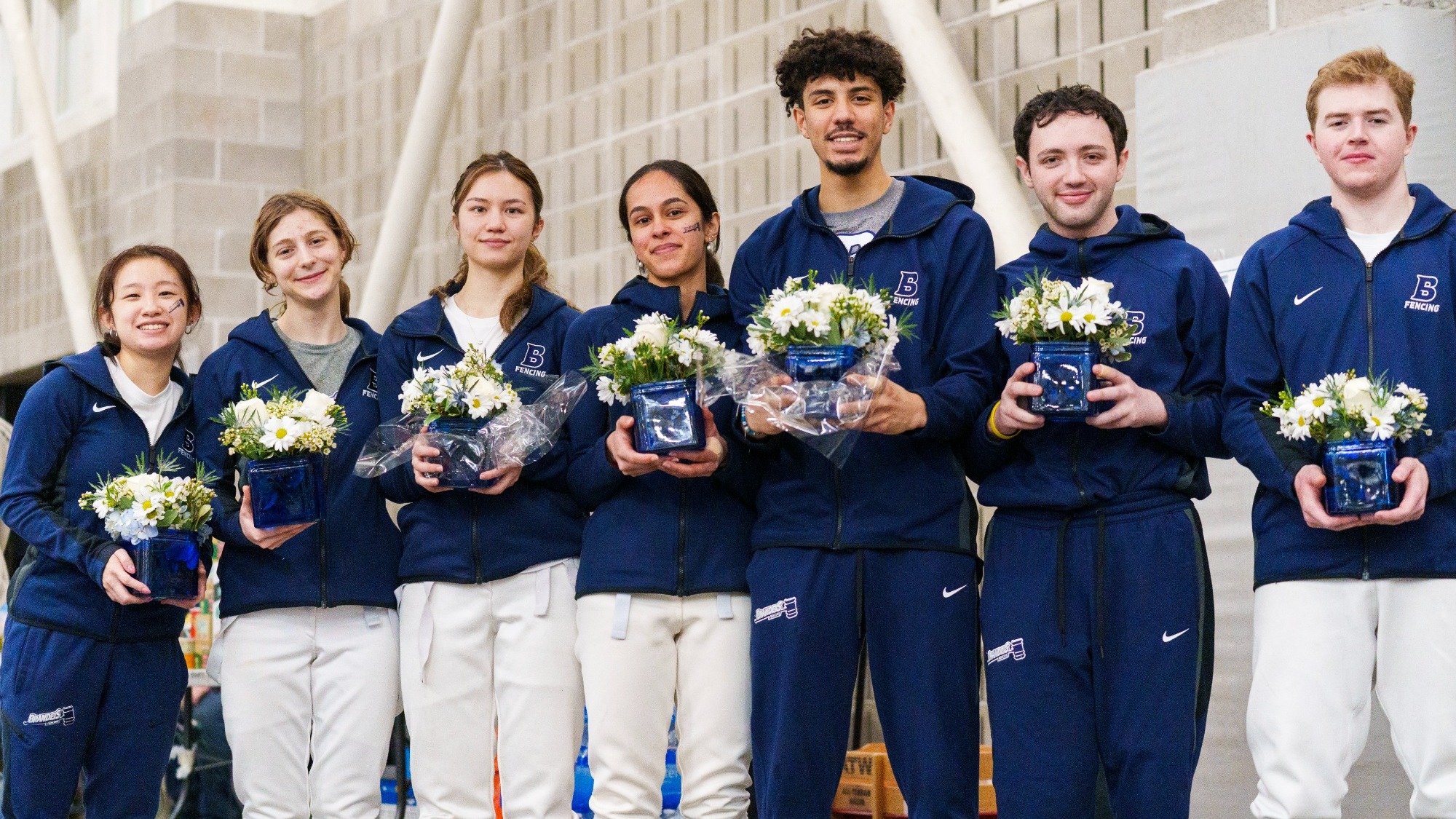 Seven Brandeis Fencing seniors posing for the camera holding their senior gifts