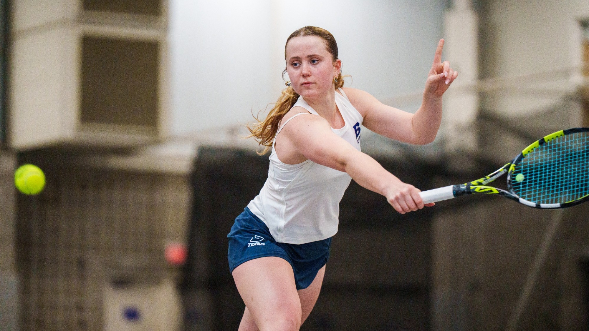 Galia Harmelin reaches for a backhand during a tennis match, but is pointing her other finger to indicate the shot was out