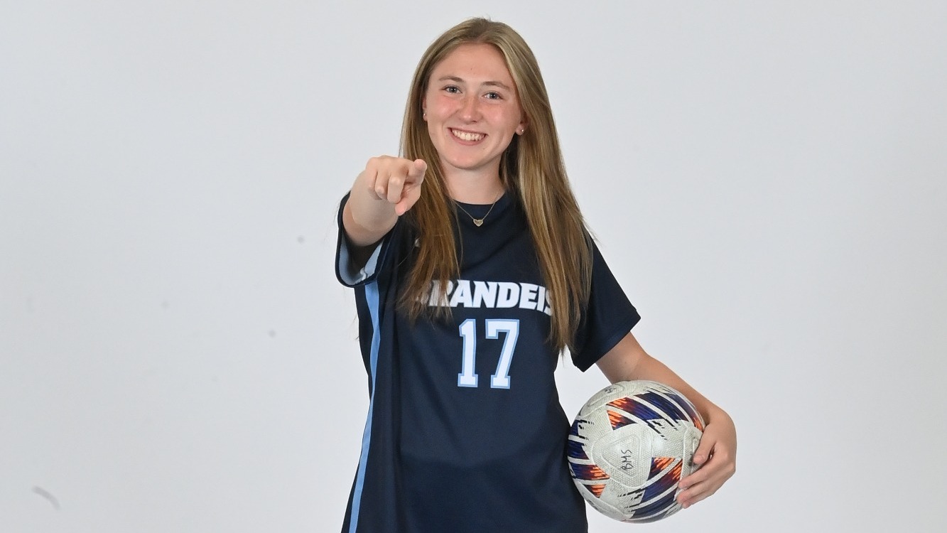 Ella Kauffman holds a soccer ball in one hand and points at the camera with the other