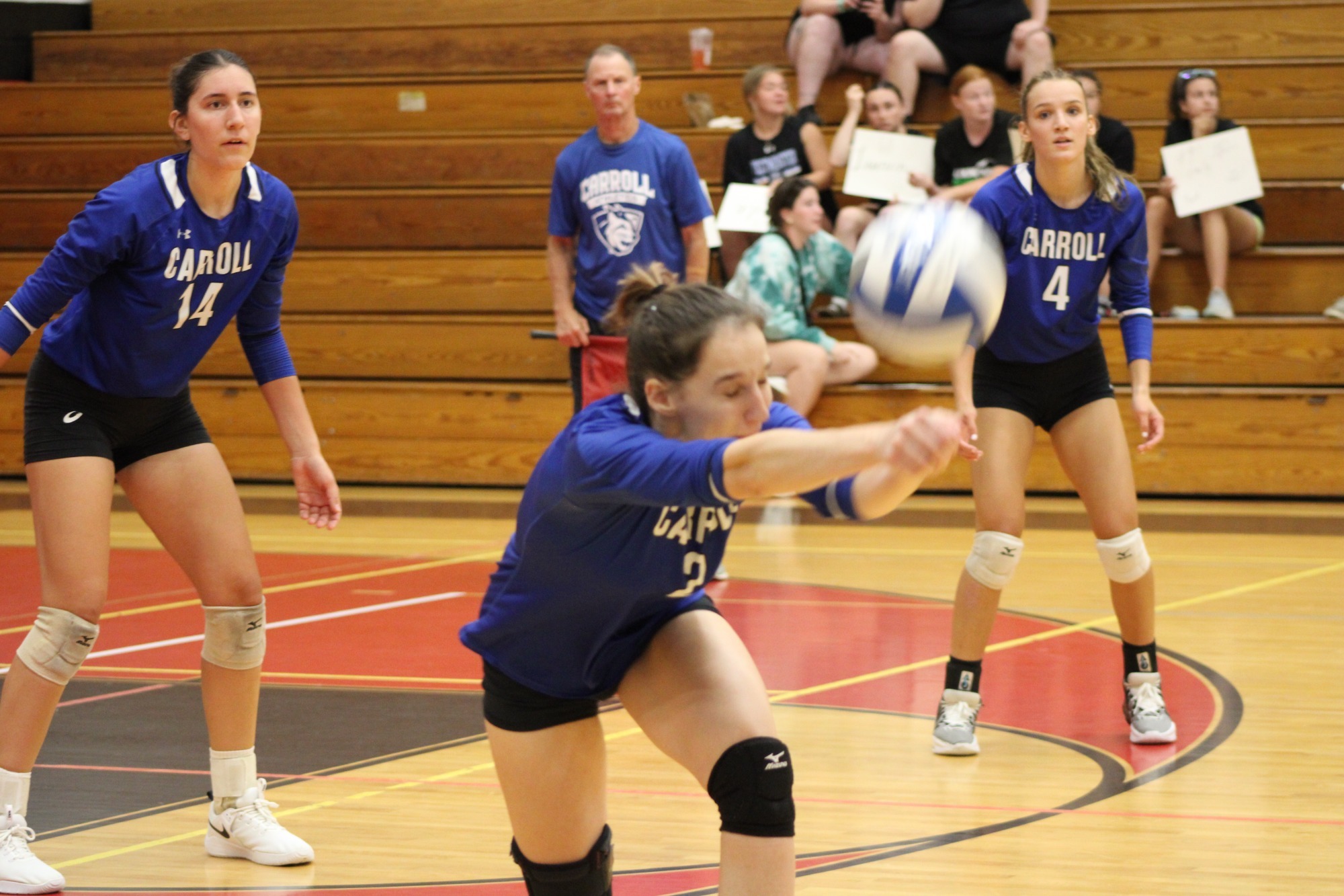 Volleyball player hits the ball with two players looking on