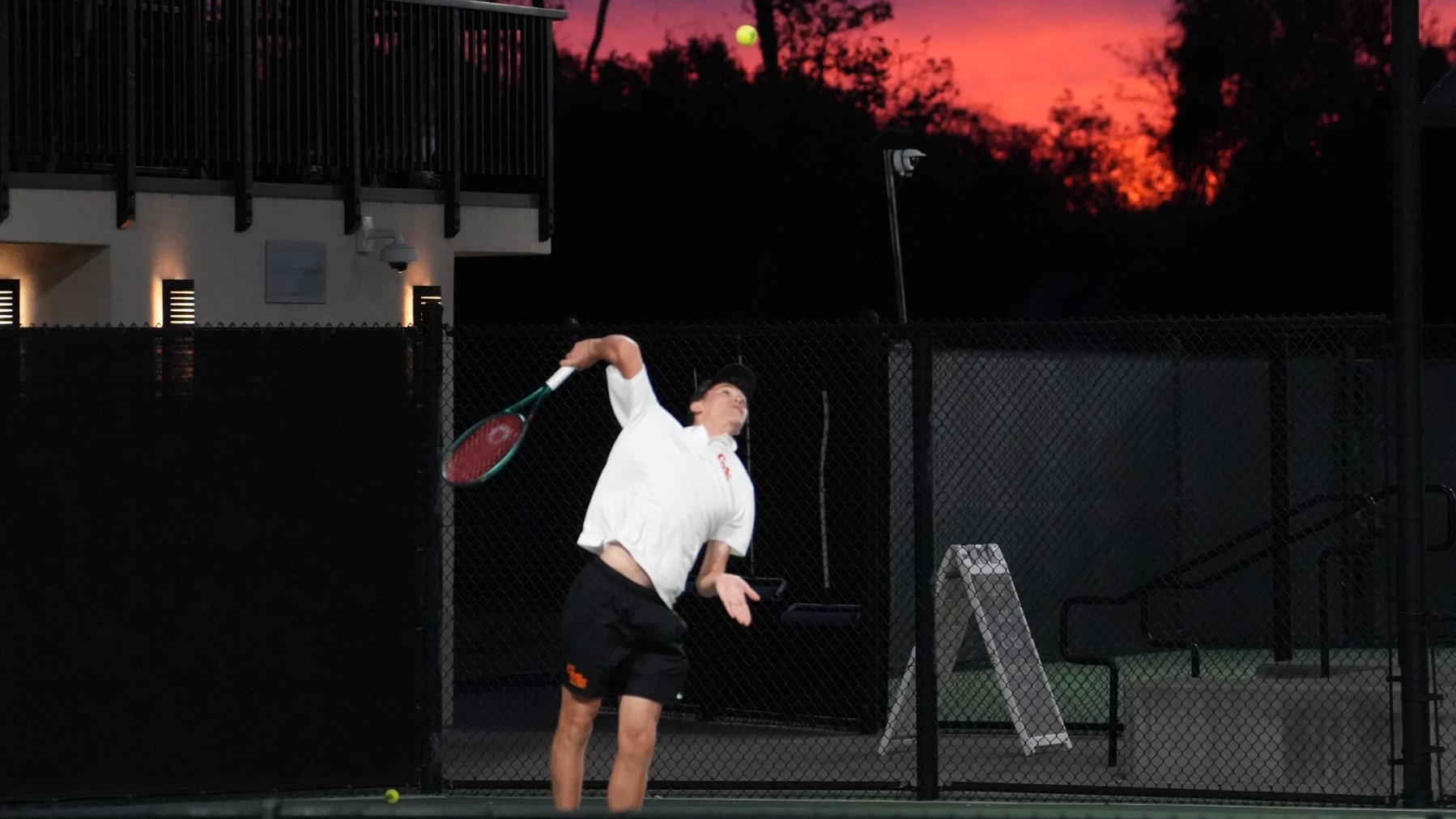 Henry Wilson serving with a sunset behind him