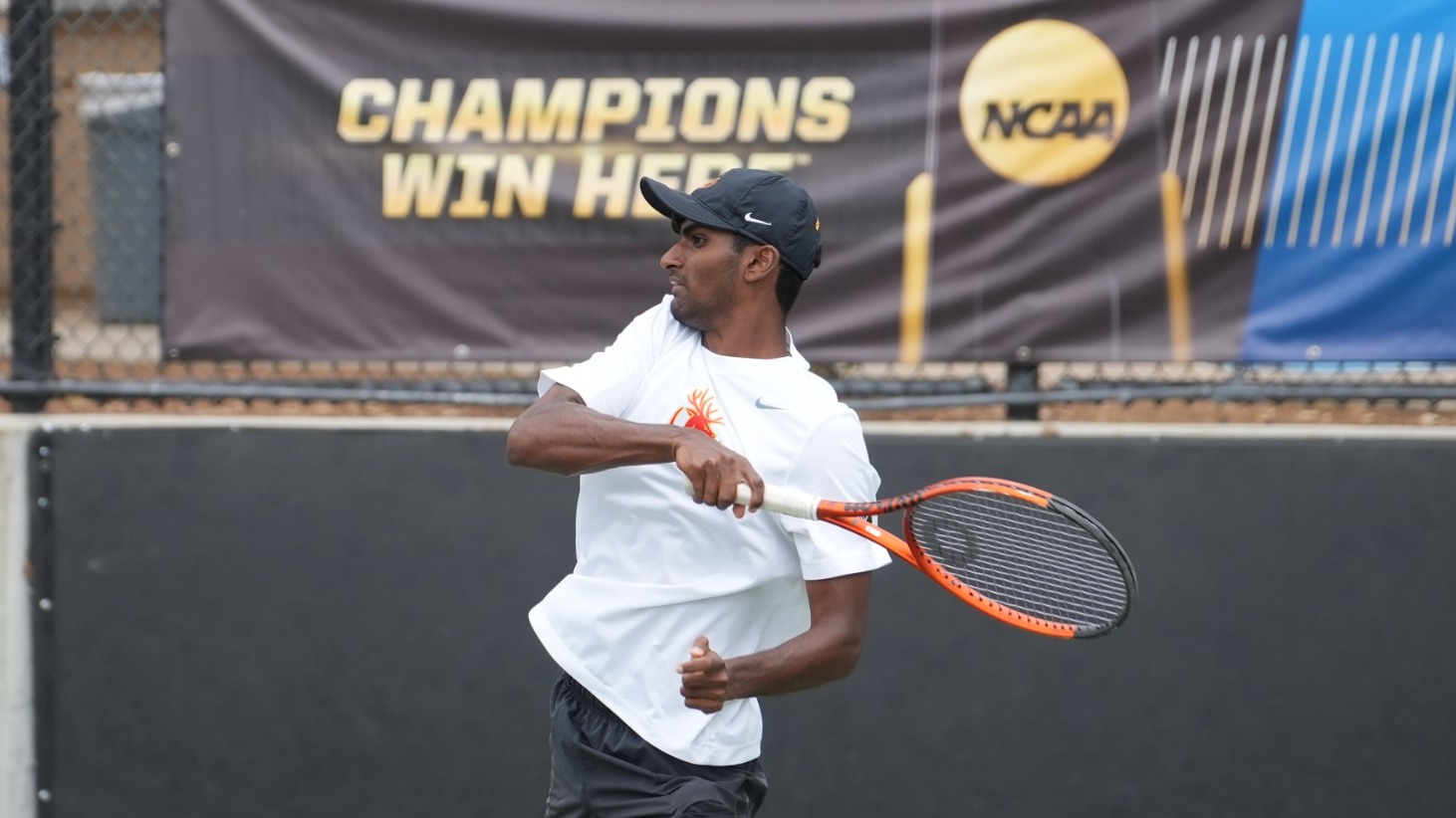 Advik Mareedu hitting a forehand with the NCAA banner 