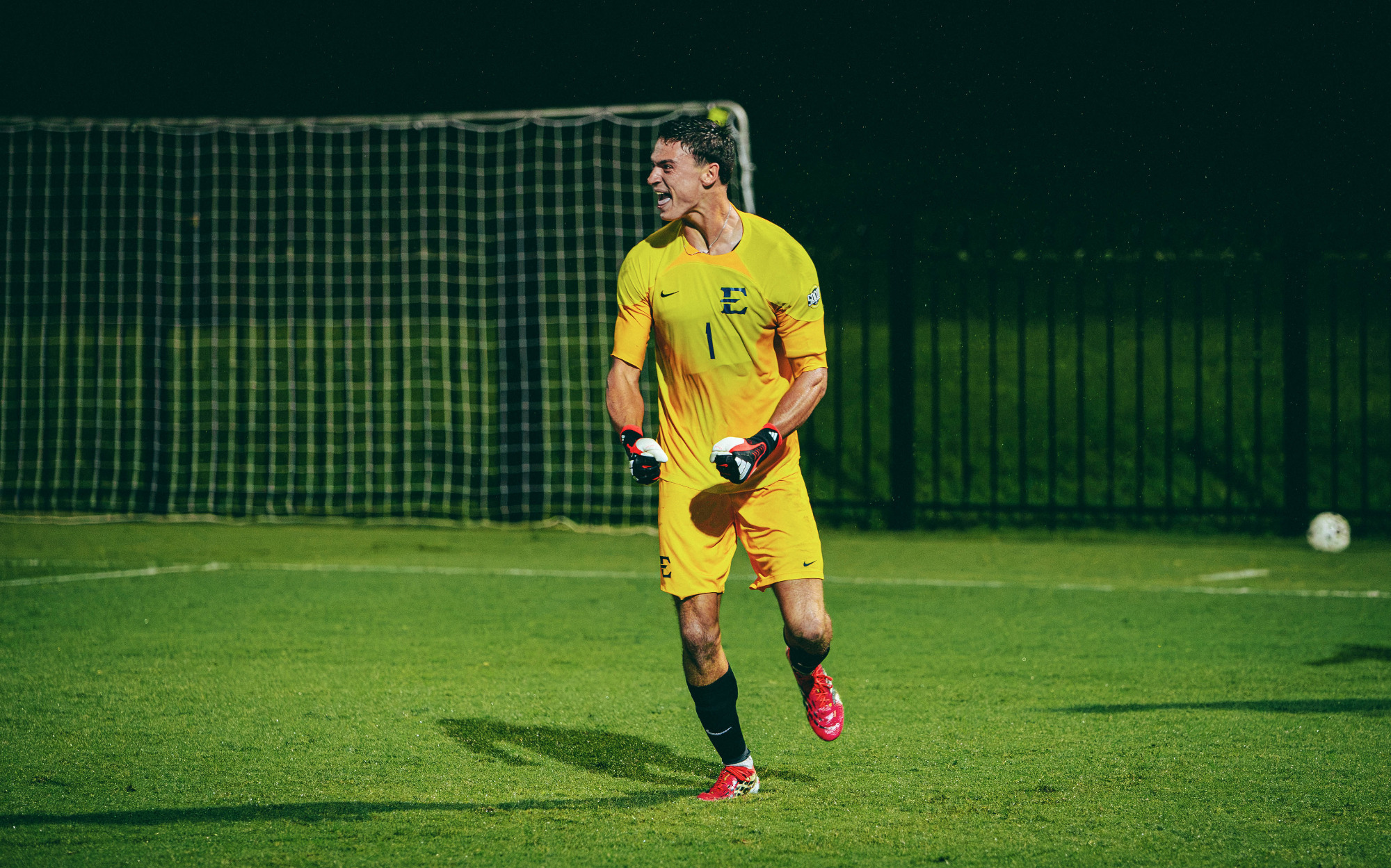 Noé Delmotte celebrates his team's win over Liberty in a soccer match, flexing his arms in his gold-colored goalkeeper uniform.