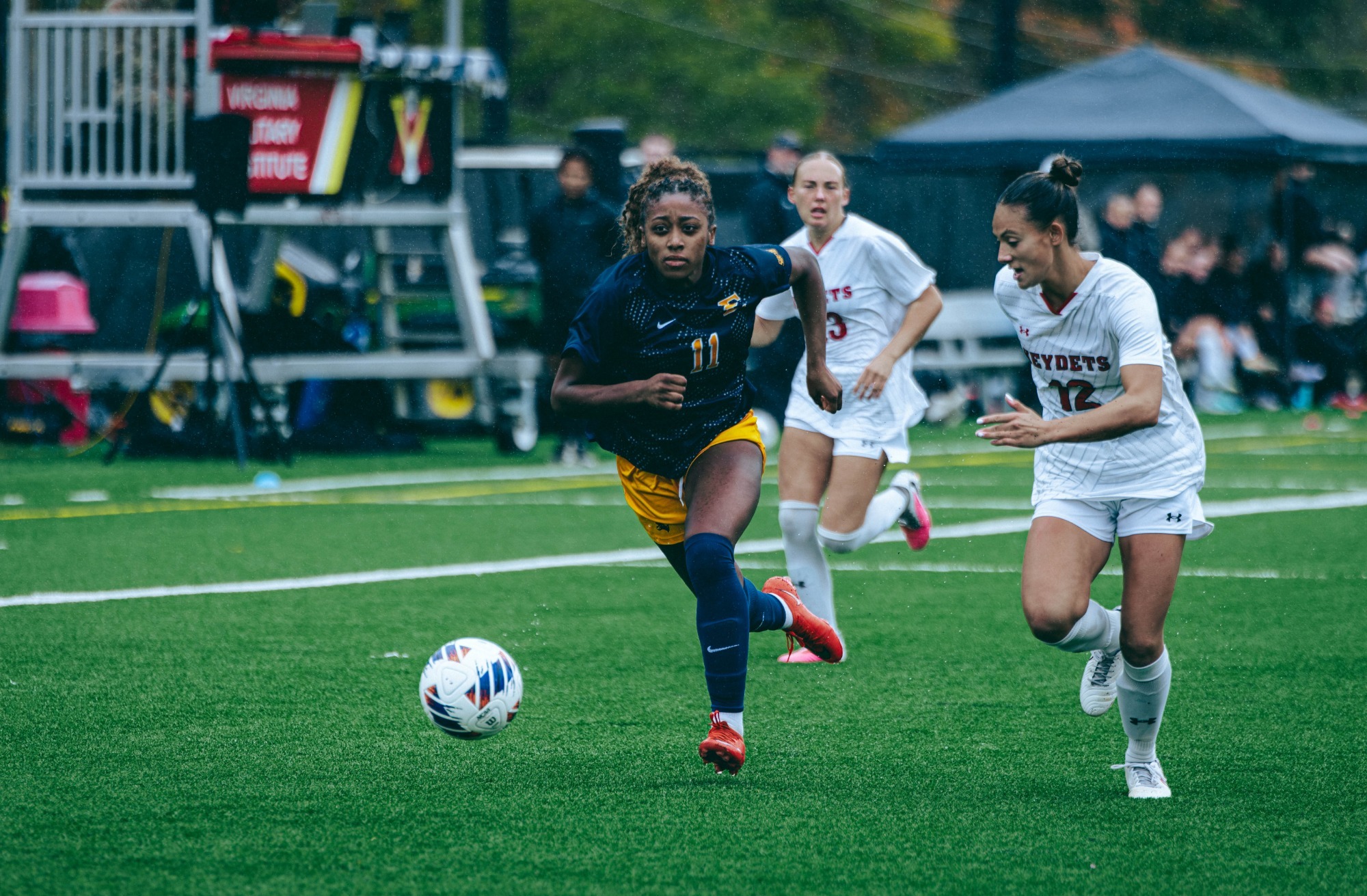 Jada Cooper runs past two VMI defenders to chase the ball during a soccer match.