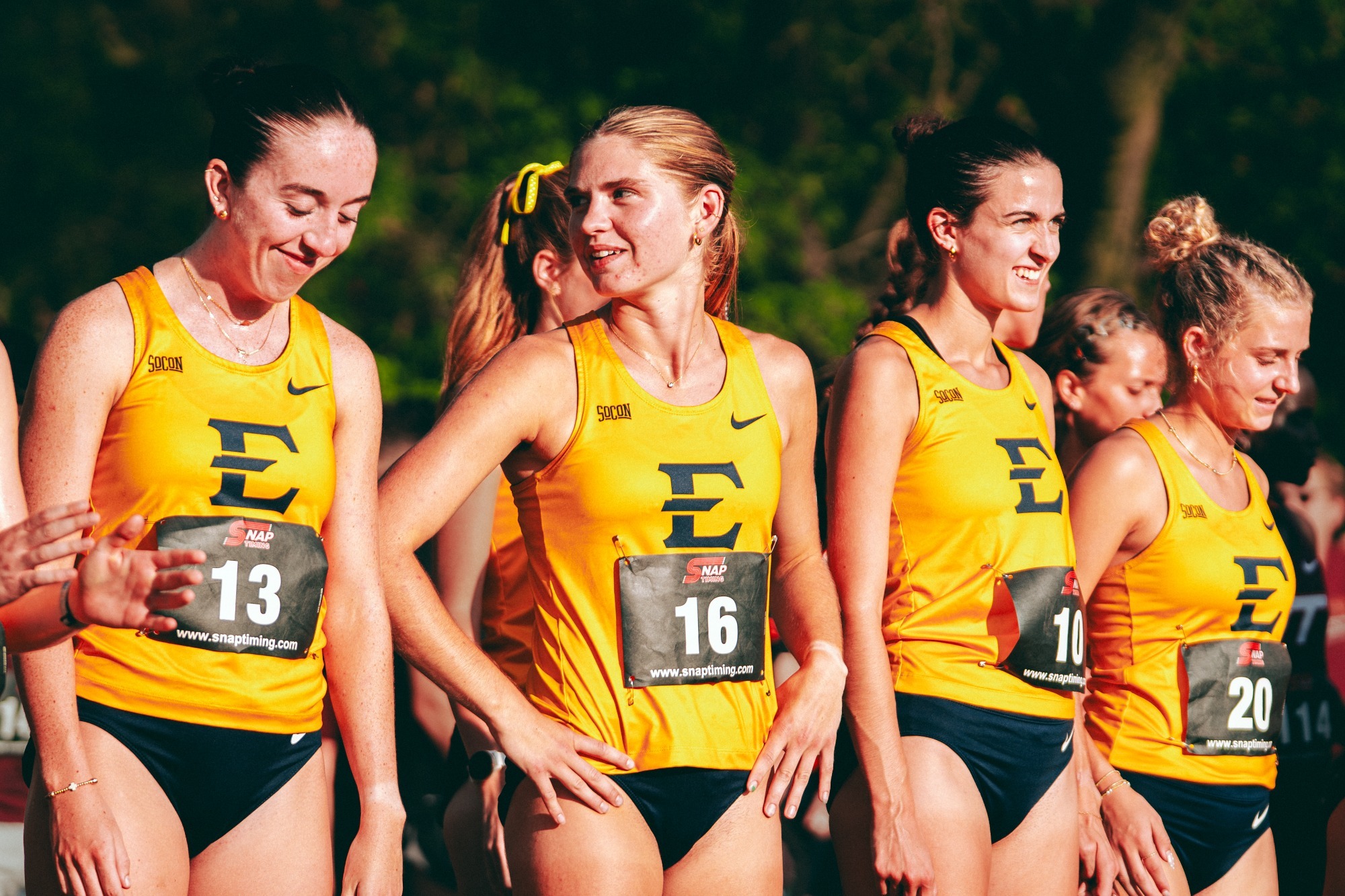 Four runners stand at the starting line before a cross country race. From left to right: McKenzie Fitzgerald, Deena Ludtke, Mackenzie Armstrong, and AJ Thomas