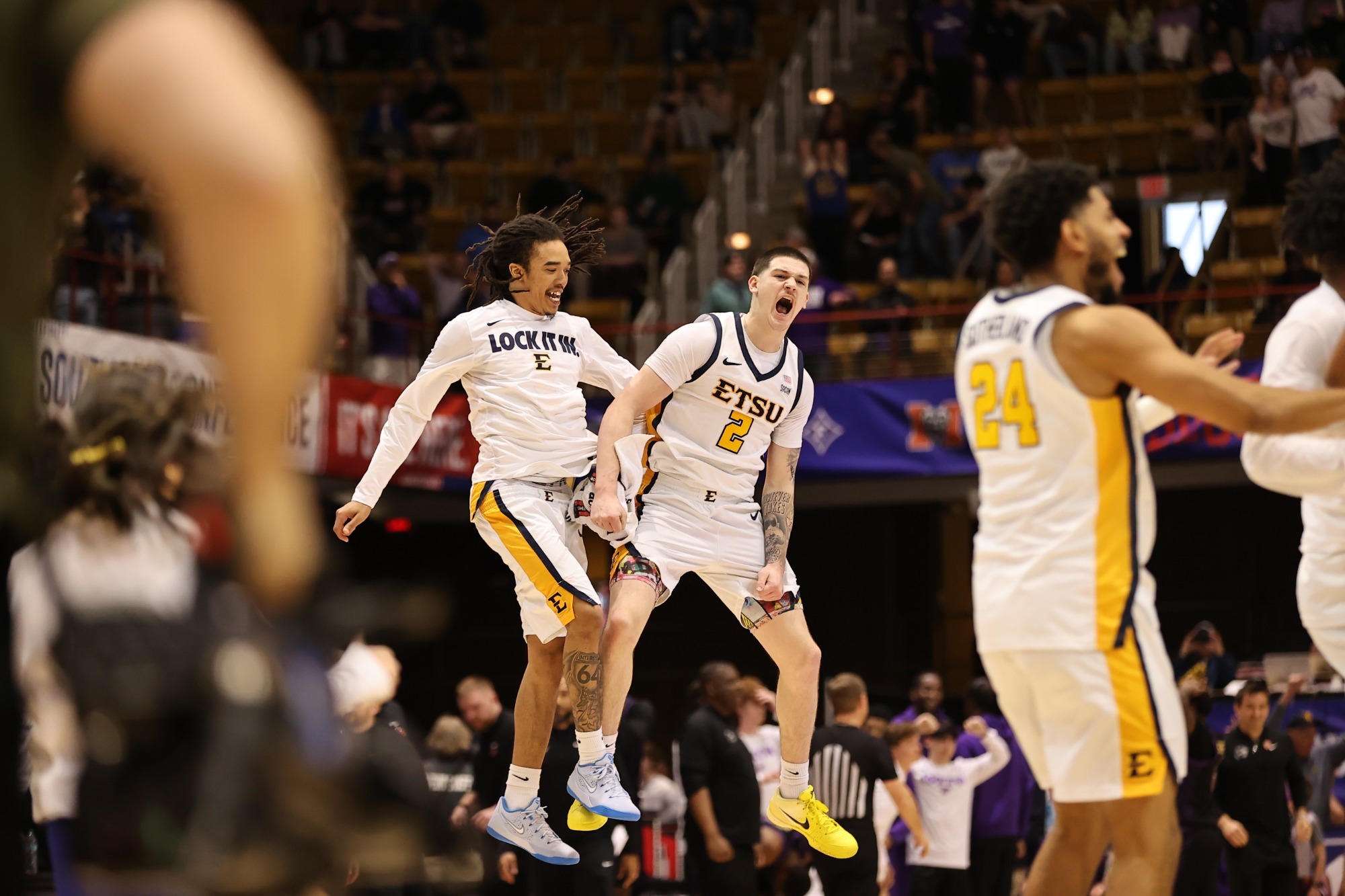 Allen Strothers on the left and Maki Johnson on the right, in their white basketball uniforms, jump in the air together to celebrate a dramatic win against Western Carolina.