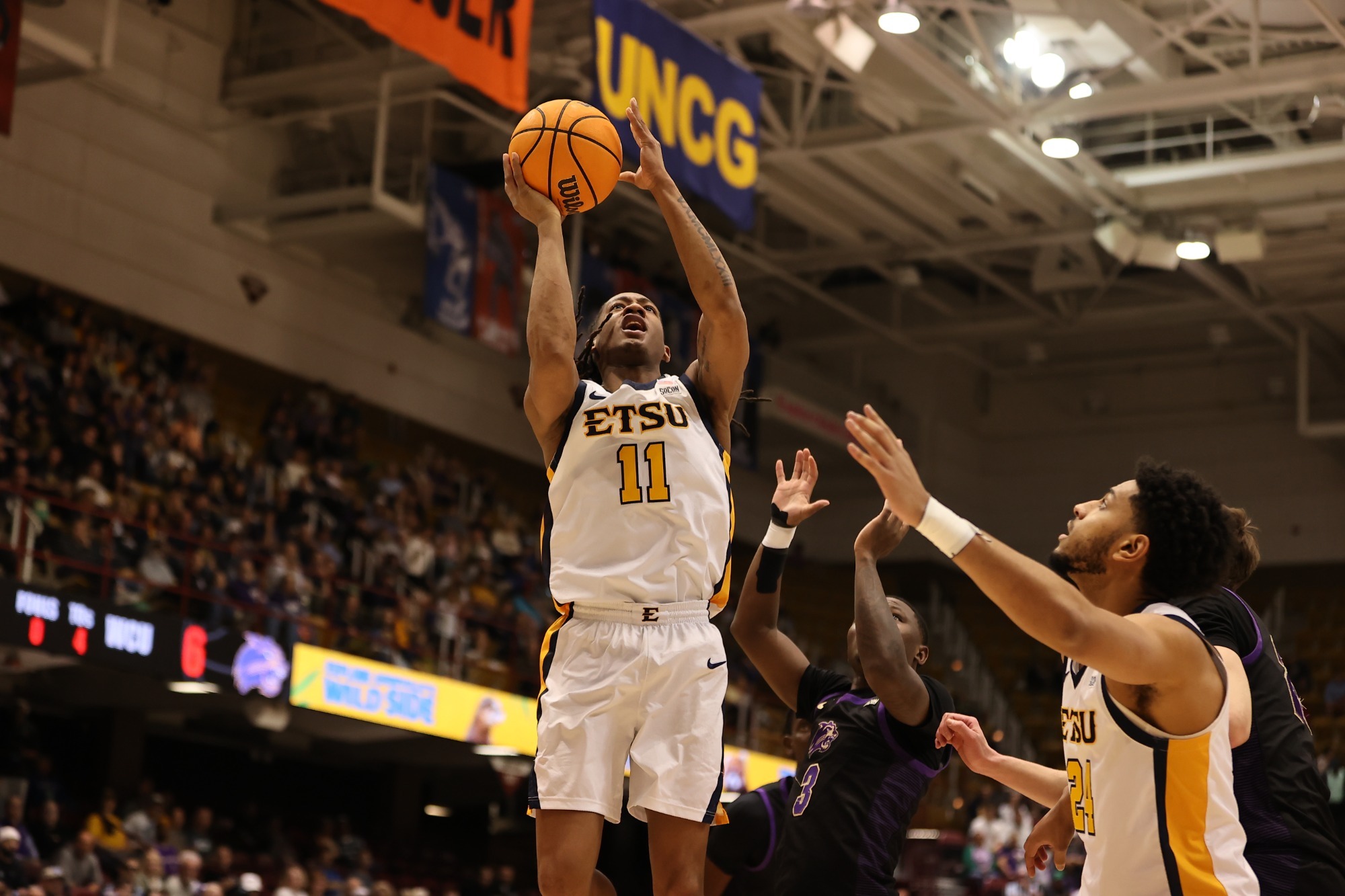 Brian Taylor, in his white basketball uniform, rises above a Western Carolina defender in black and purple with the basketball in his right hand for a layup.