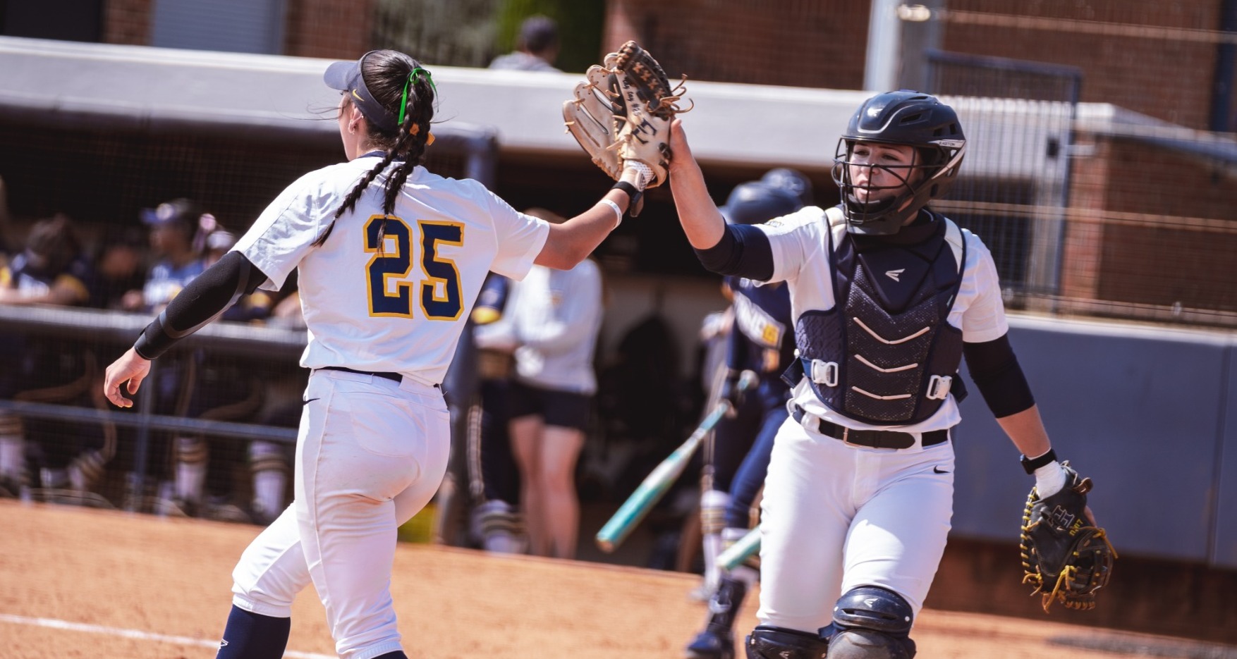 Softball's Taylor Suchy (pitcher) and Leinani Lutu (catcher) touching gloves after making an out.