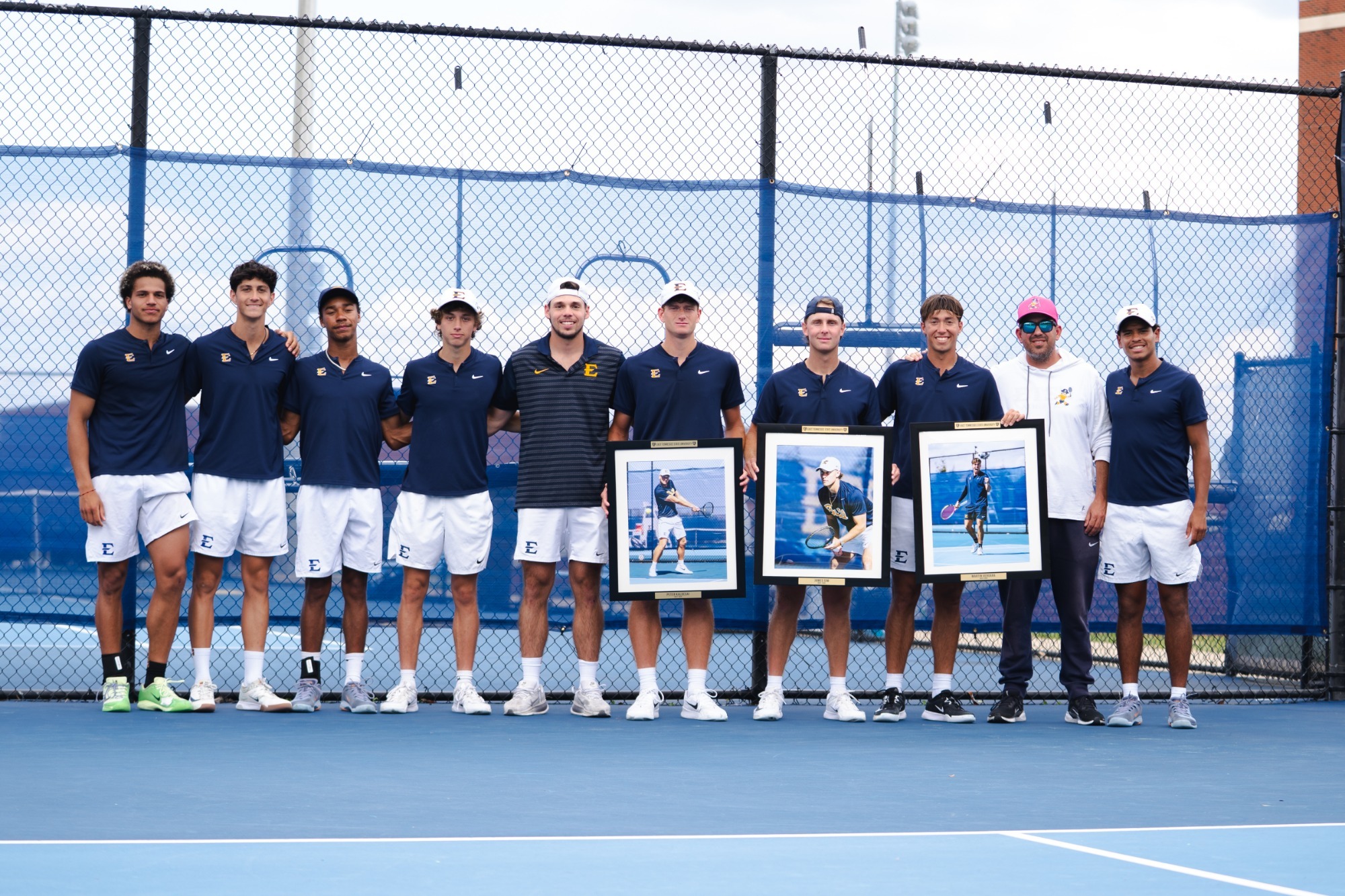 ETSU men's tennis seniors Peter Kalocsai, James Sim, and Martin Vergara are recognized during their match against Chattanooga. These three are joined for a photo with the coaching staff and the rest of the Buccaneers. 