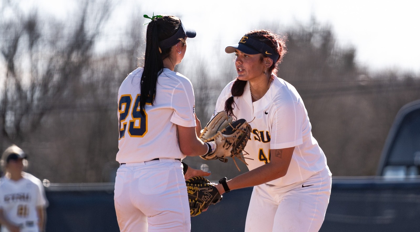 ETSU softball players Taylor Suchy and Riley Martens touching gloves on the pitchers mound while Suchy pitches and Martens plays first.