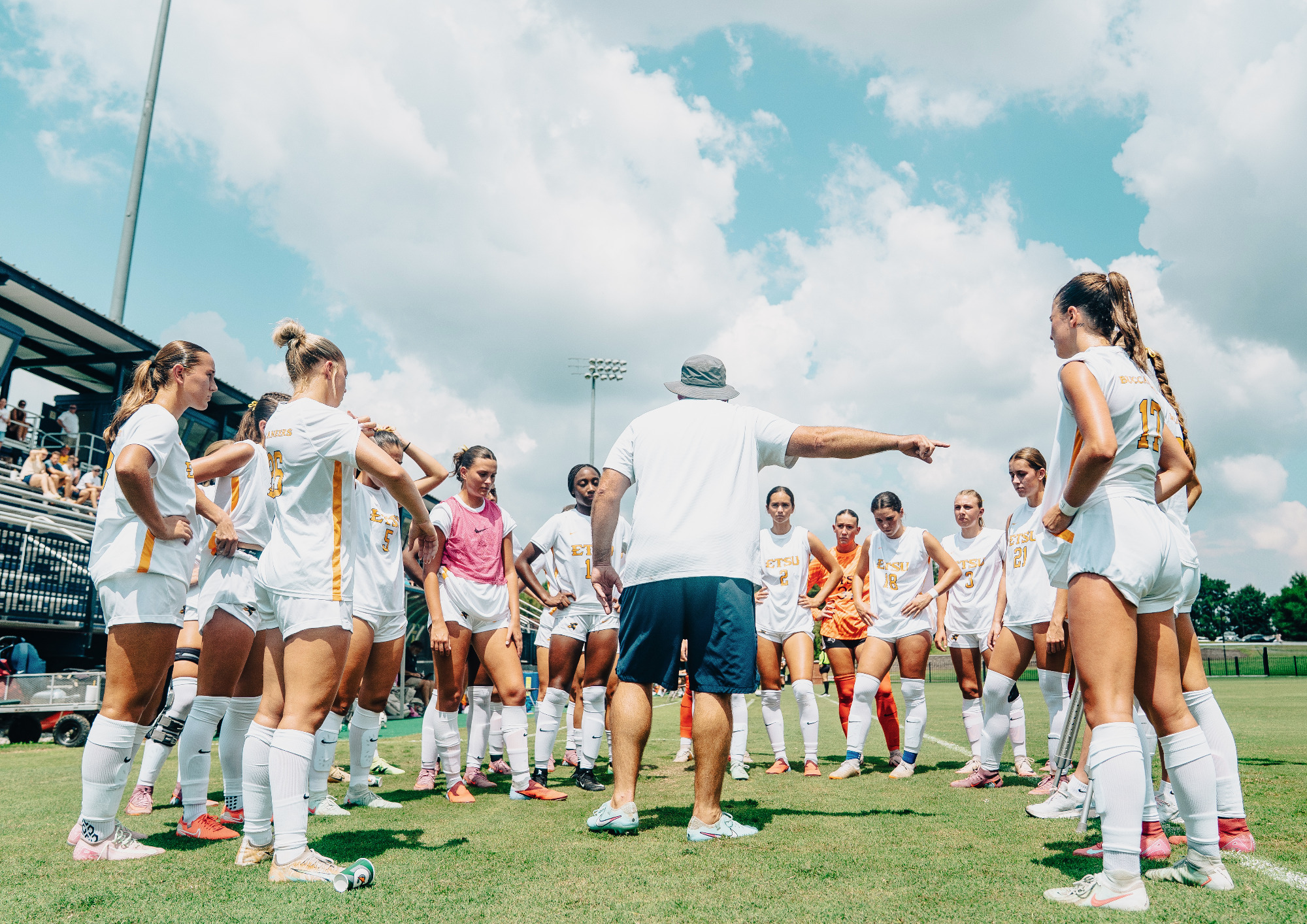 Jay Yelton talks to his soccer team in a pregame huddle before a game. The team surrounds him in their home white uniforms.