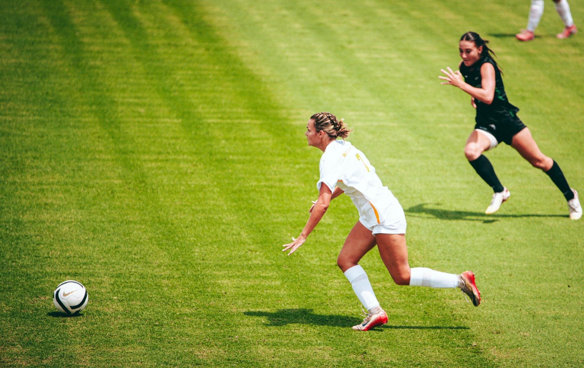 McKlain Jones in her white home uniform dribbles away from a defender during a soccer match with USC Upstate.