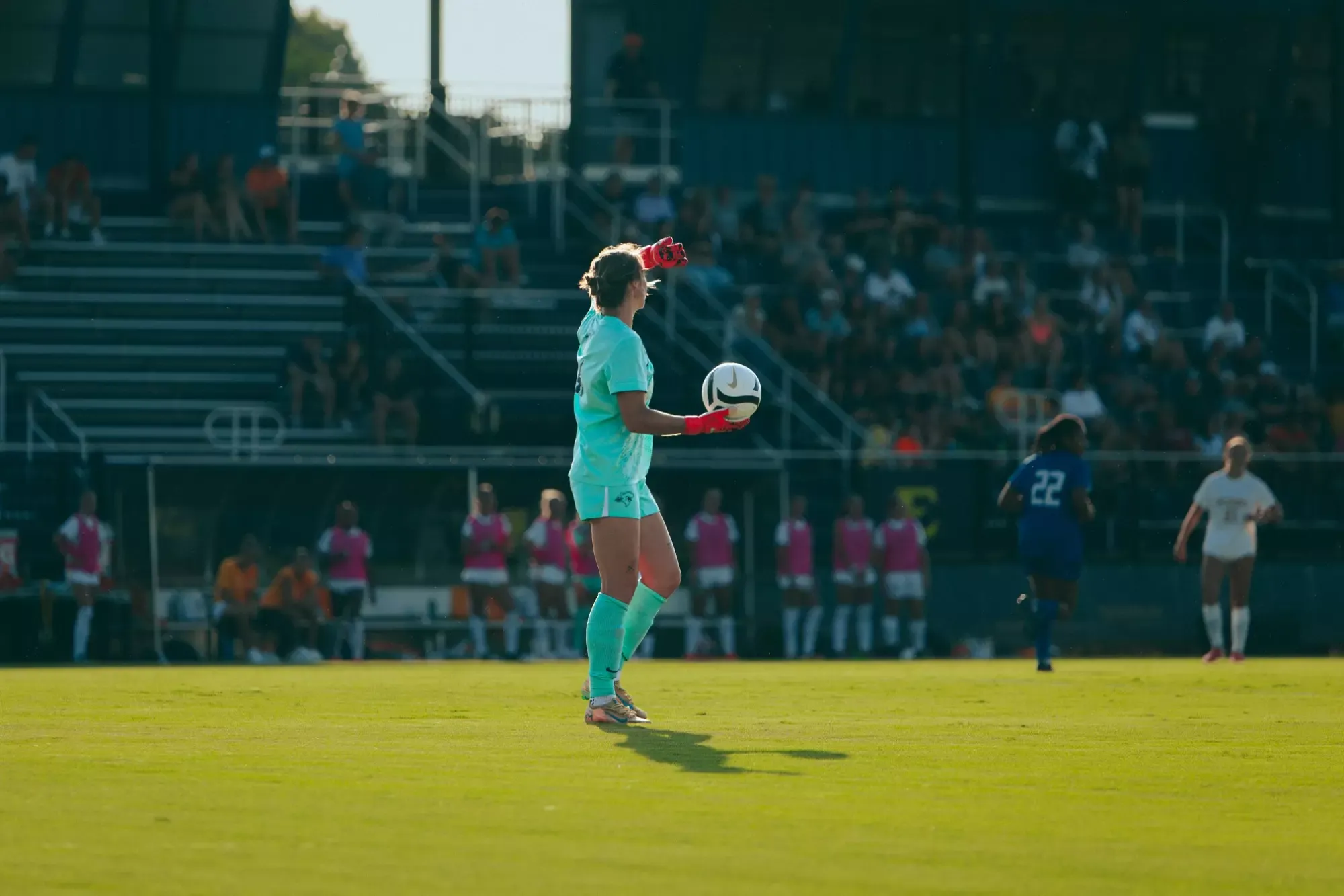 Addison Yelton, in her teal goalkeeper's uniform, holds the ball inside the 18-yard box during a soccer match