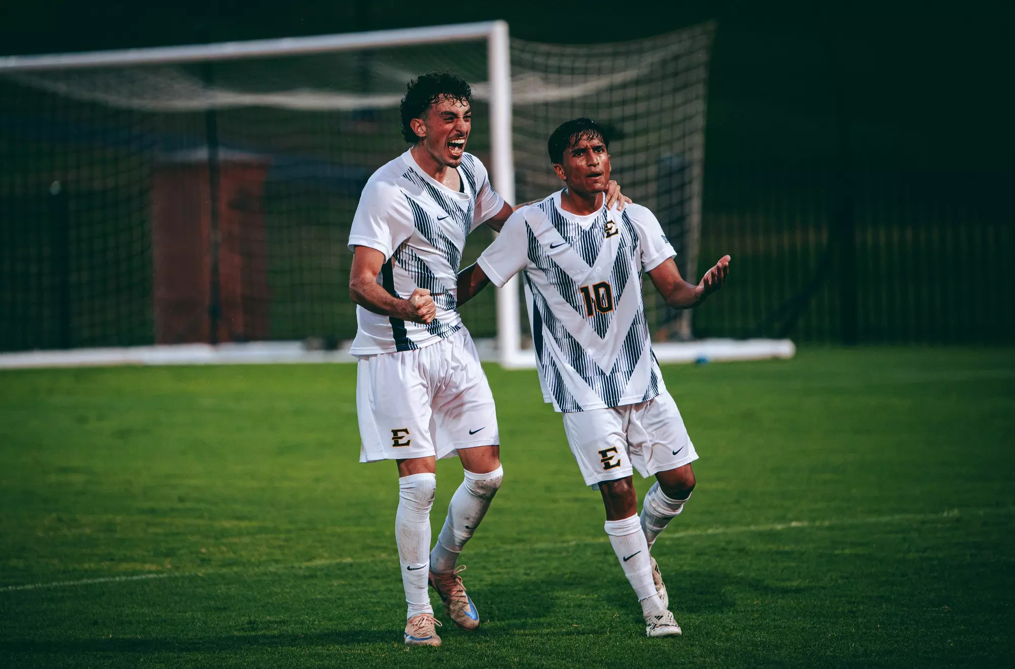 Jaime Carrillo holds his arms out to celebrate a goal against Belmont. Matias Delellis joins him from the viewer's left with his left arm around Carrillo's shoulders.