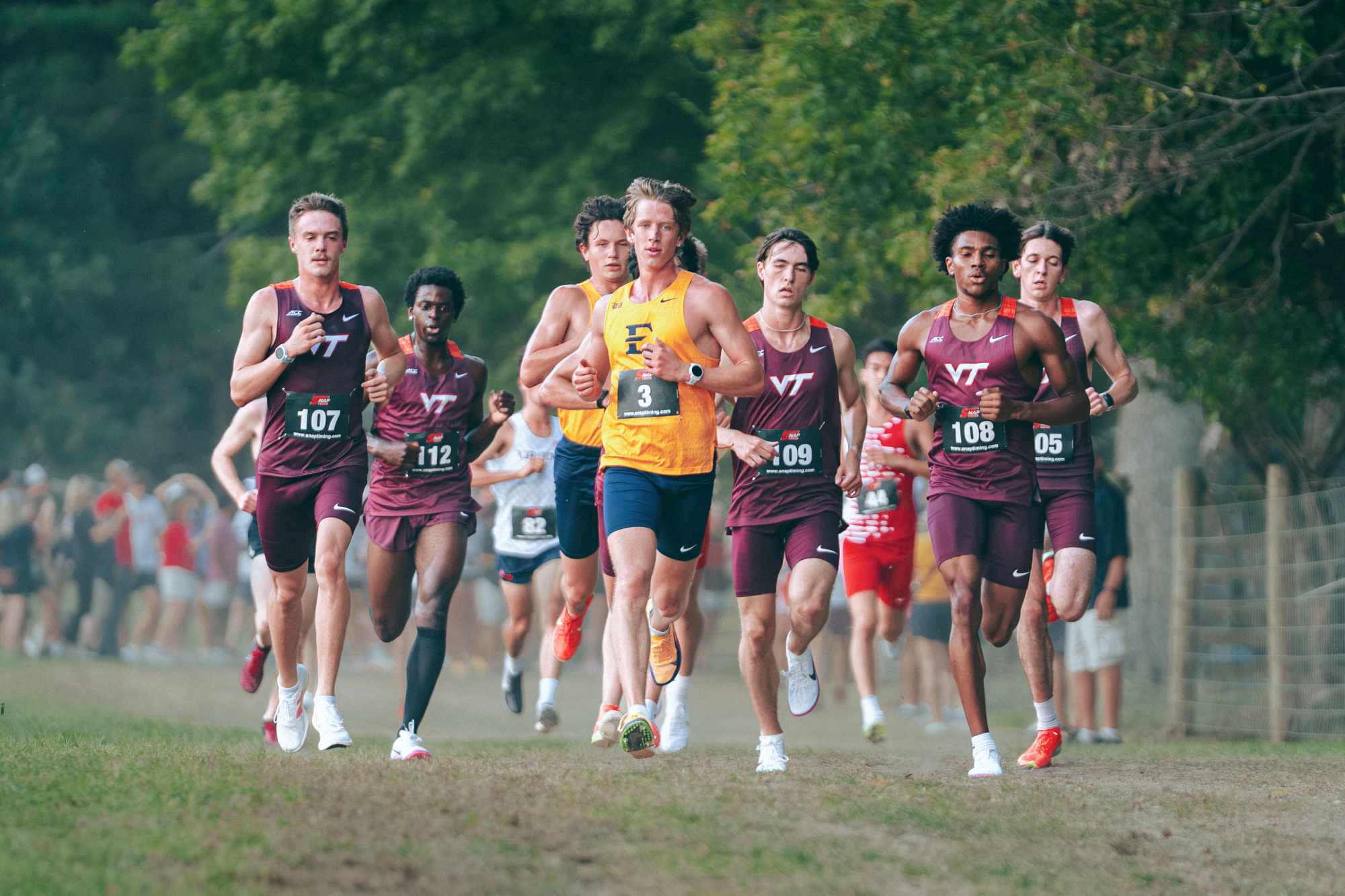 Garrett Hawkins leads a pack of runners during a cross country race in Blacksburg, Virginia. His blue and gold racing uniform stands out in front of the burgundy uniforms of the pack of competitors behind him.
