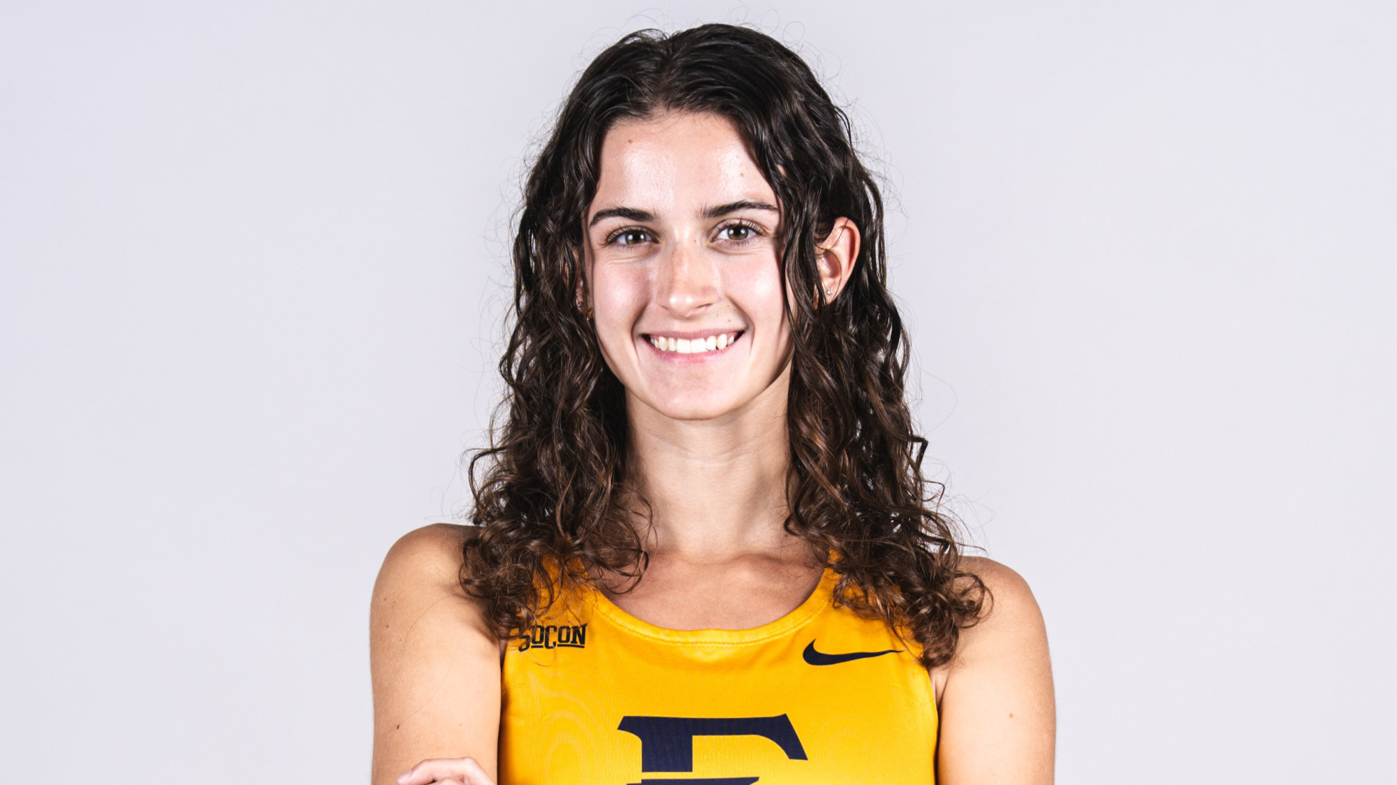 A medium shot of Mackenzie Armstrong in her cross country uniform in front of a gray background.