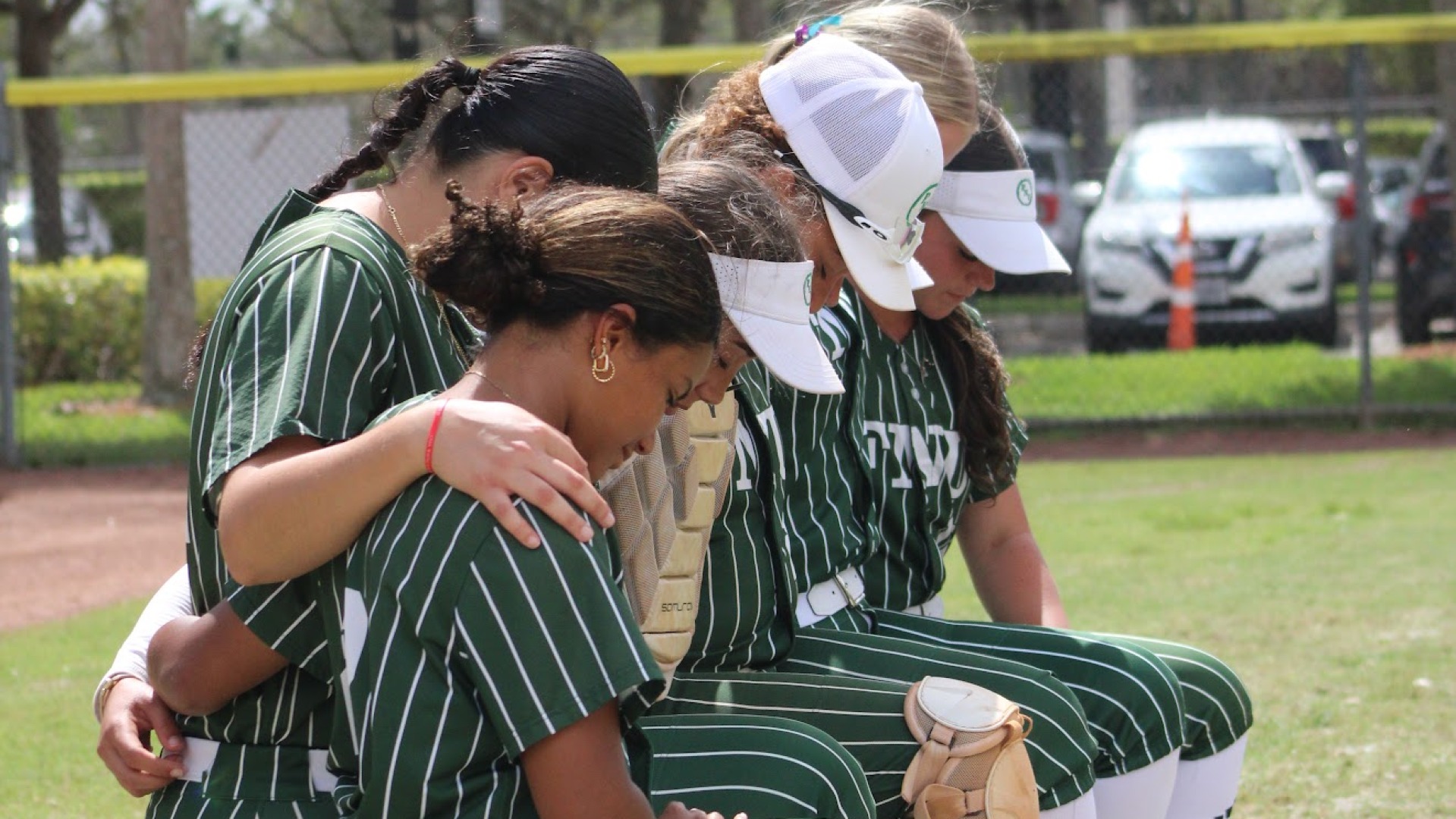 Softball players kneeling in prayer before a home game 2026