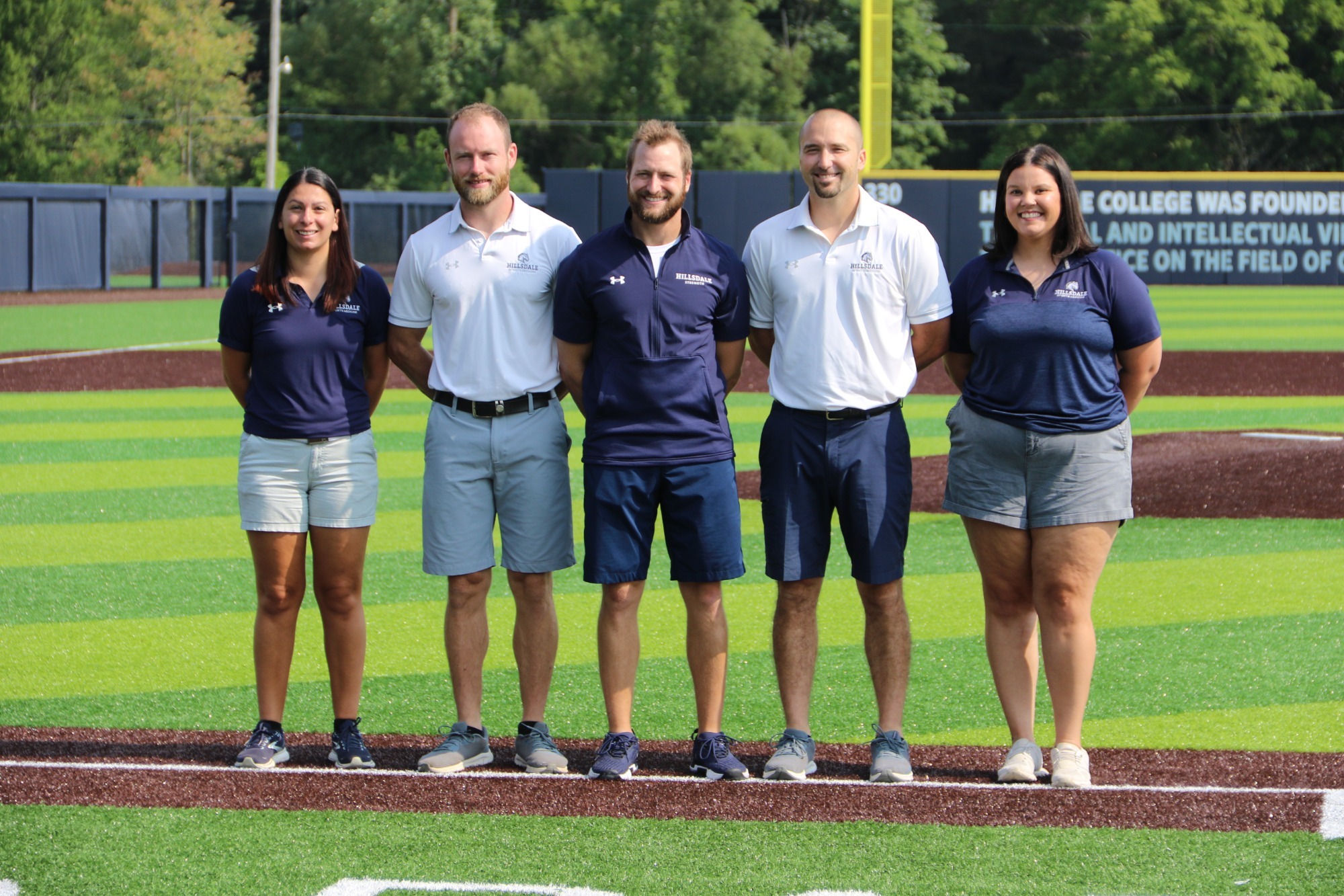 Hillsdale College staff (from left) Jordyn Dubina, Dan Hudson, Mitchell Schoenborn, Tyler Cortright and Mikayla Kemp pose for a photo at the Lenda and Glenda Hill Baseball Stadium. Not pictured, trainers Lynne Neukom and Kelly Zdan