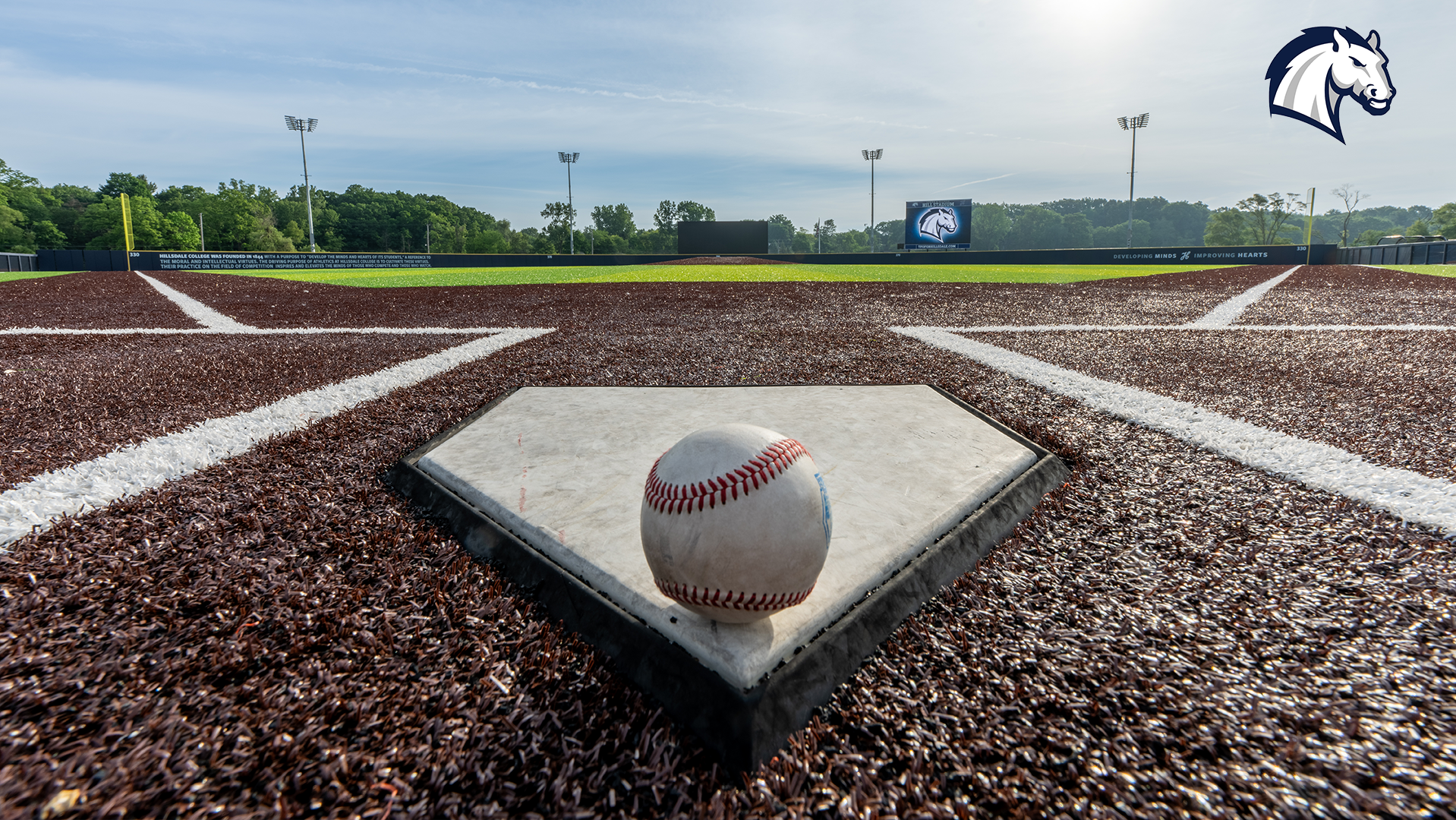 A baseball sits on home plate with Lenda and Glenda Hill Stadium and TFO Partners Field in the background.