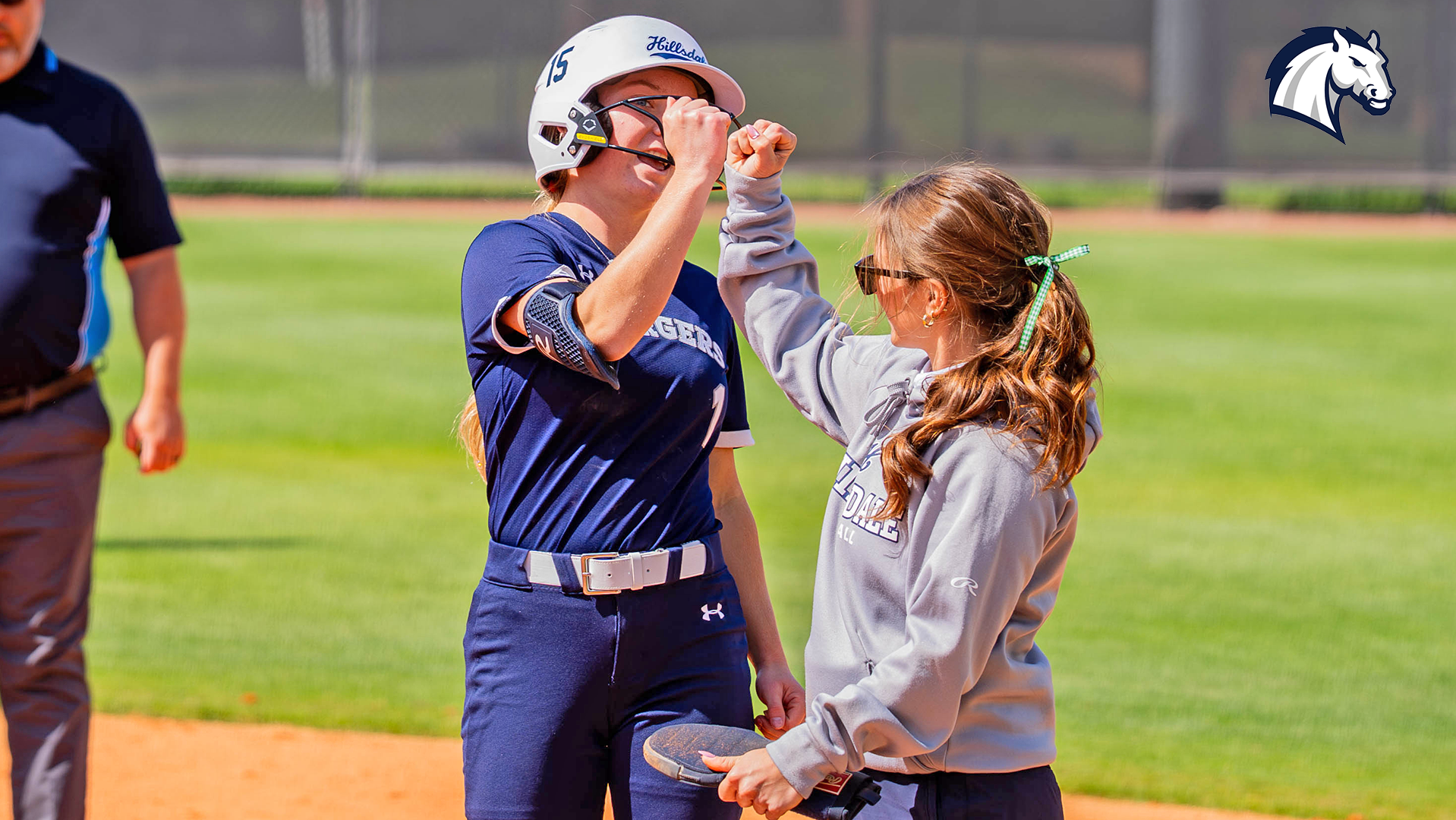 Hillsdale's Emma Sather (left) gets congratulations from assistant coach Taylor Segorski after reaching first base safely against Tampa on March 17, 2026.