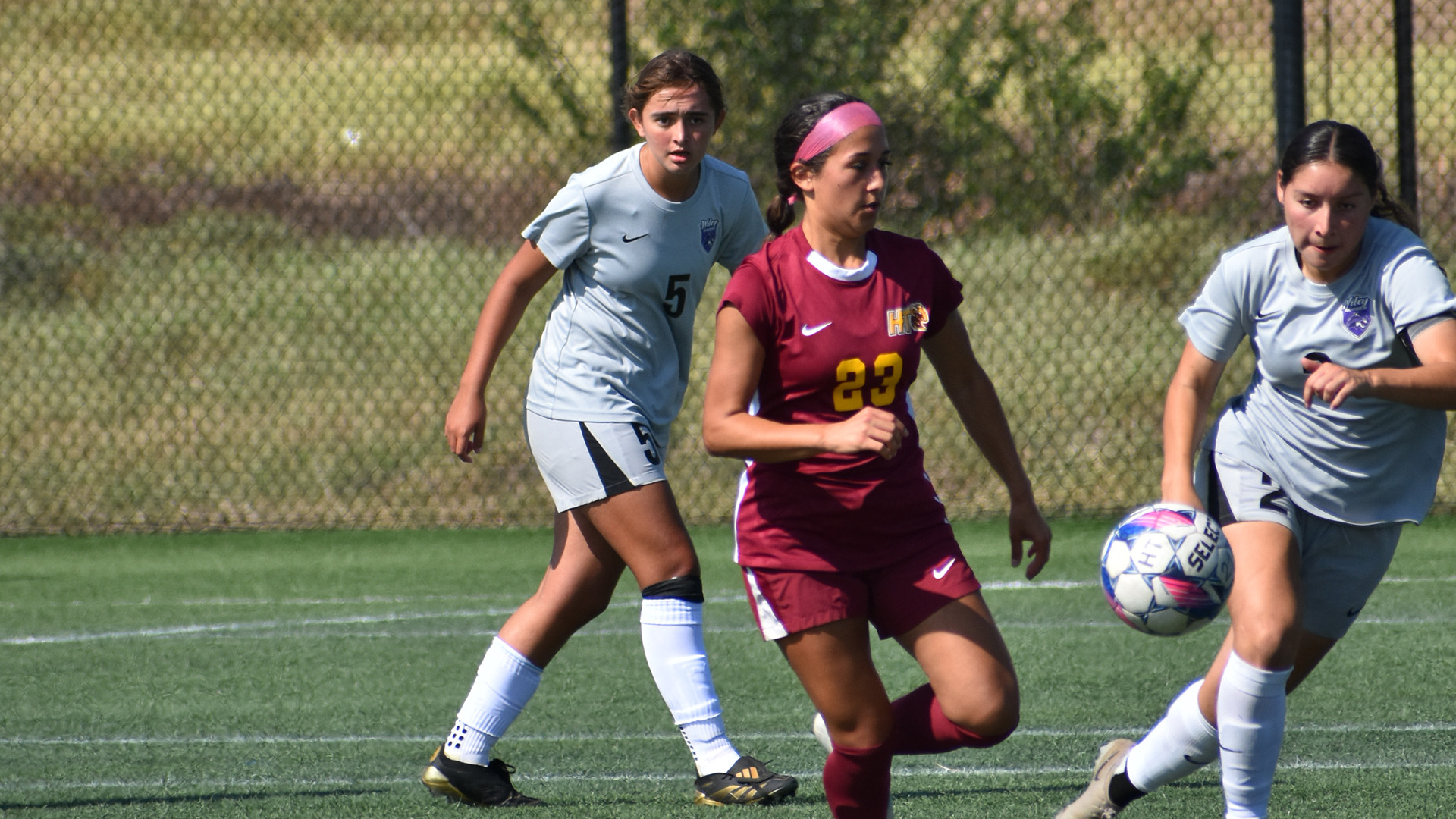 HT soccer player Caroline Valencia dribbles to elude two Wiley defenders, who are closing in on the play.