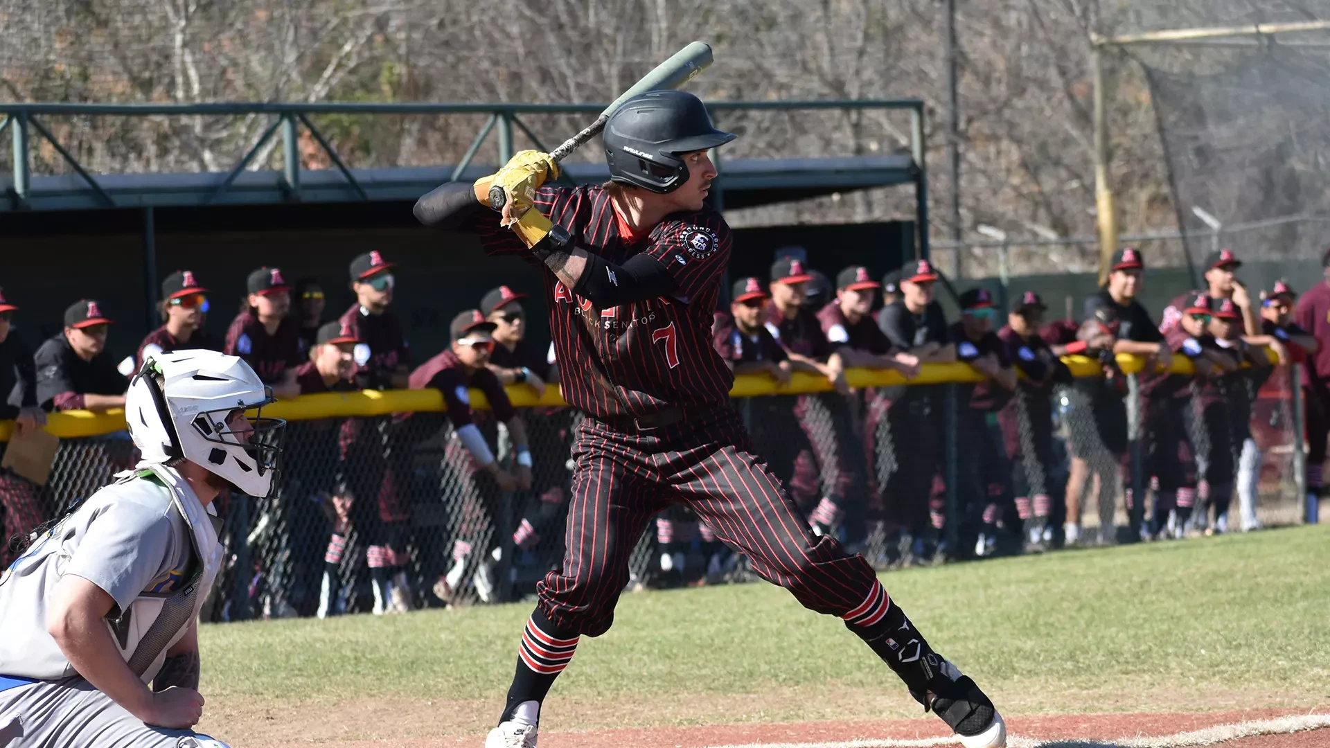 HT baseball player Tucker Allen waits for a pitch at bat against Central Christian College. HT's dugout and players are visible in the background.