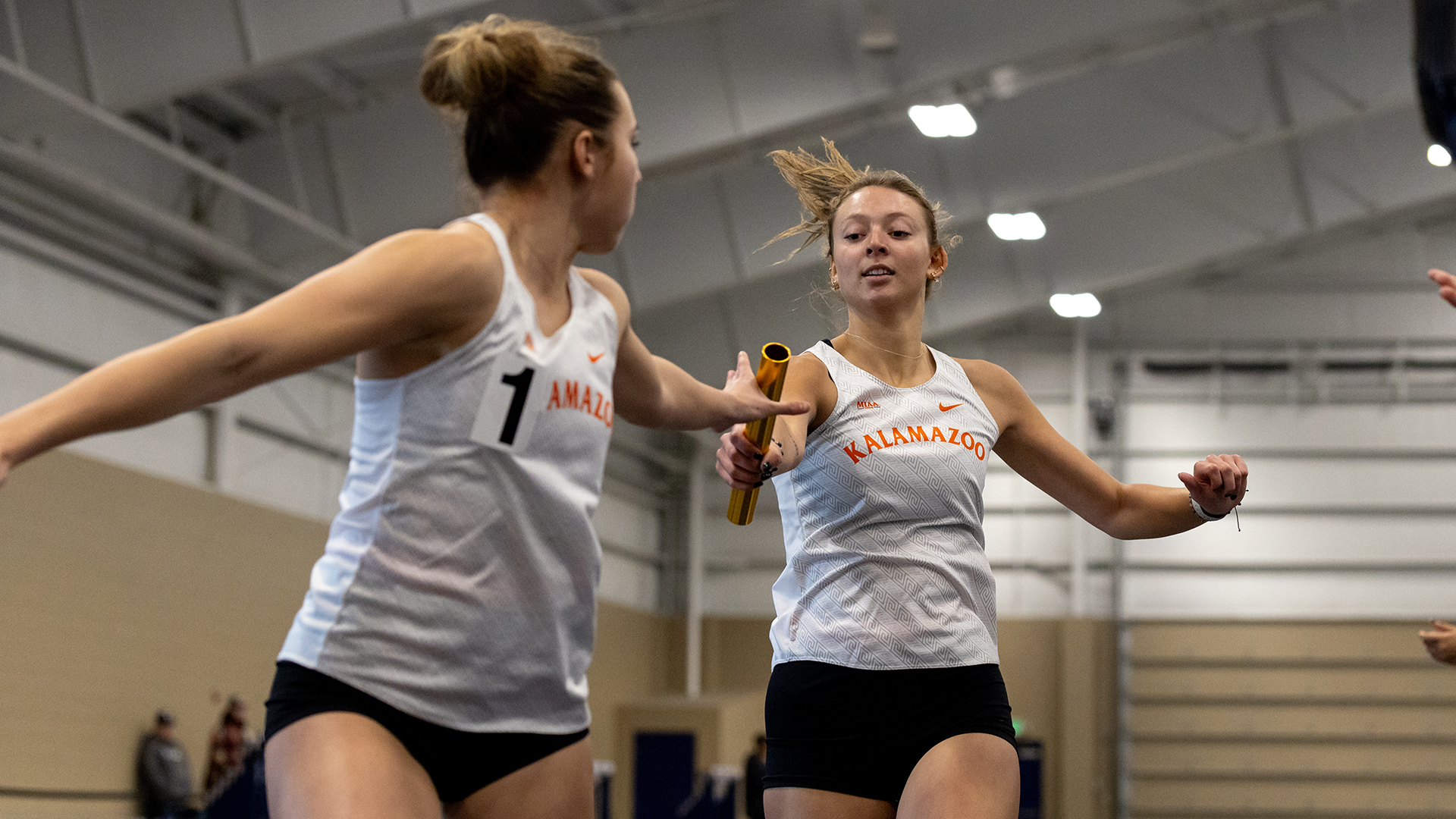 A Kalamazoo College relay team completes a baton handoff