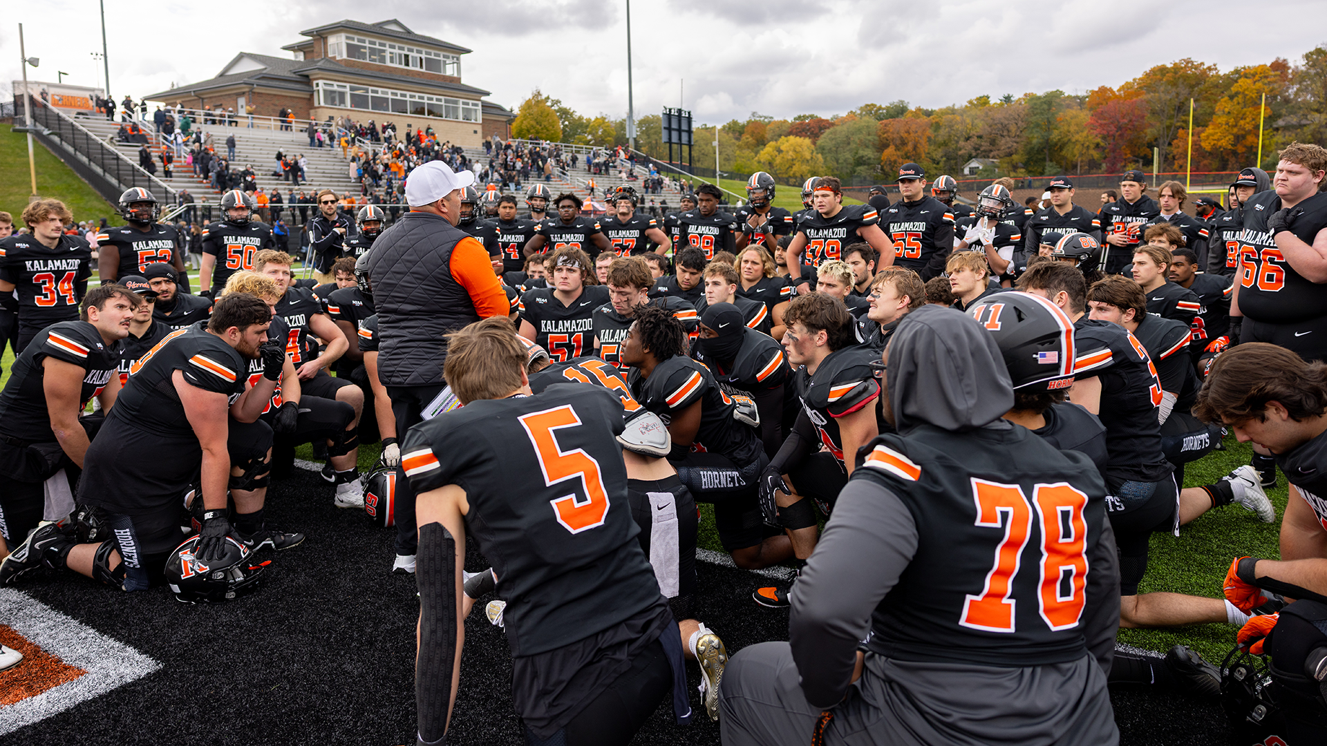 The Kalamazoo College football team kneeling while head coach Jamie Zorbo talks postgame