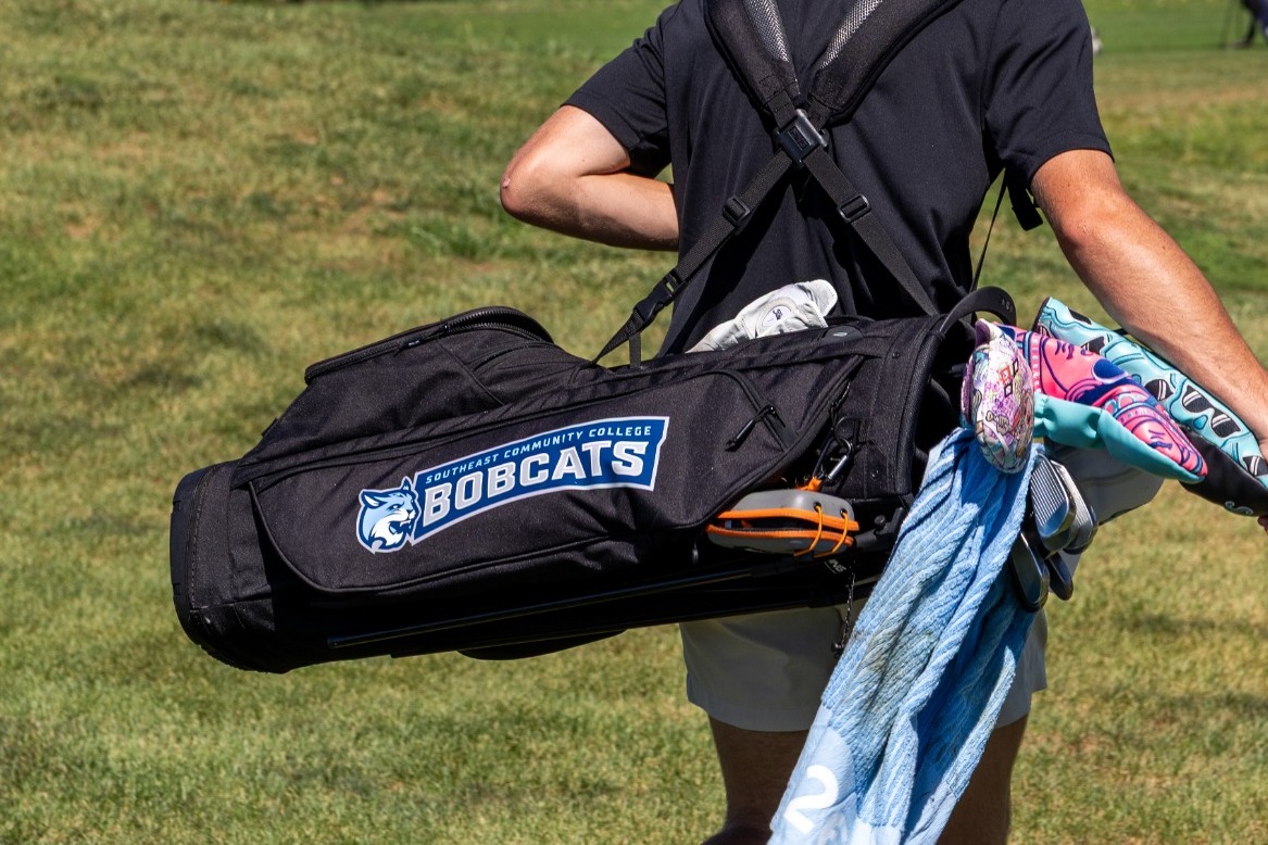 A men's golfer for SCC is seen walking away, with the Bobcats logo visible on his golf bag.