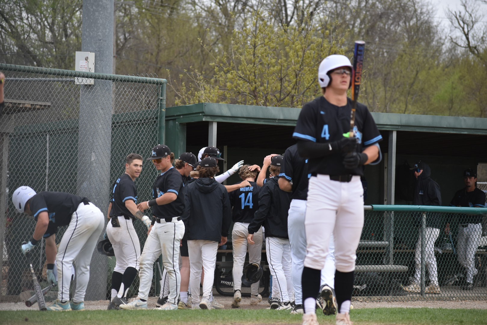 Crew Moeller stands in the foreground preparing to bat, while Jordan Monroe runs into the dugout celebration after a home run