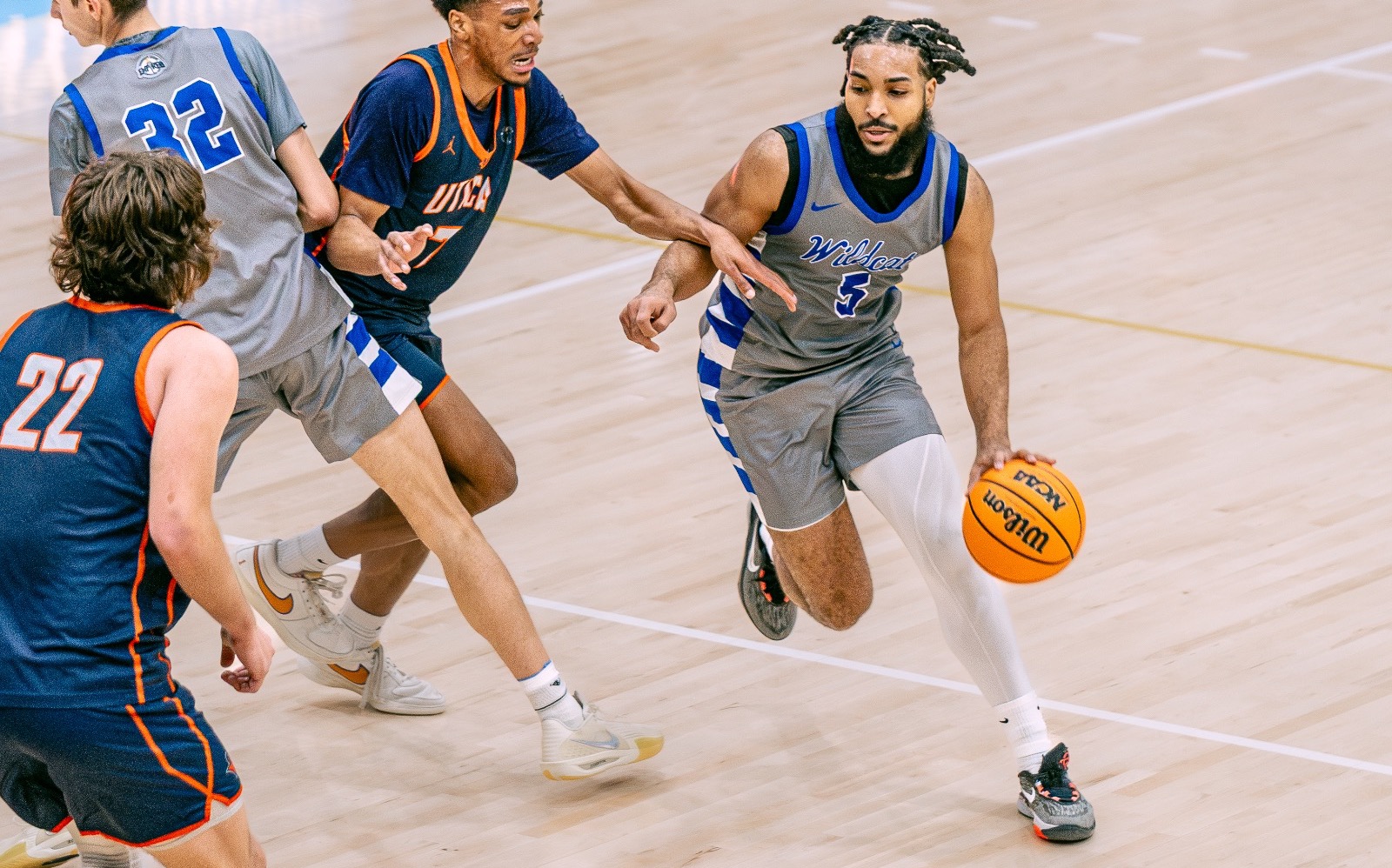 SUNY Poly men’s basketball player dribbles around screen looking for options 