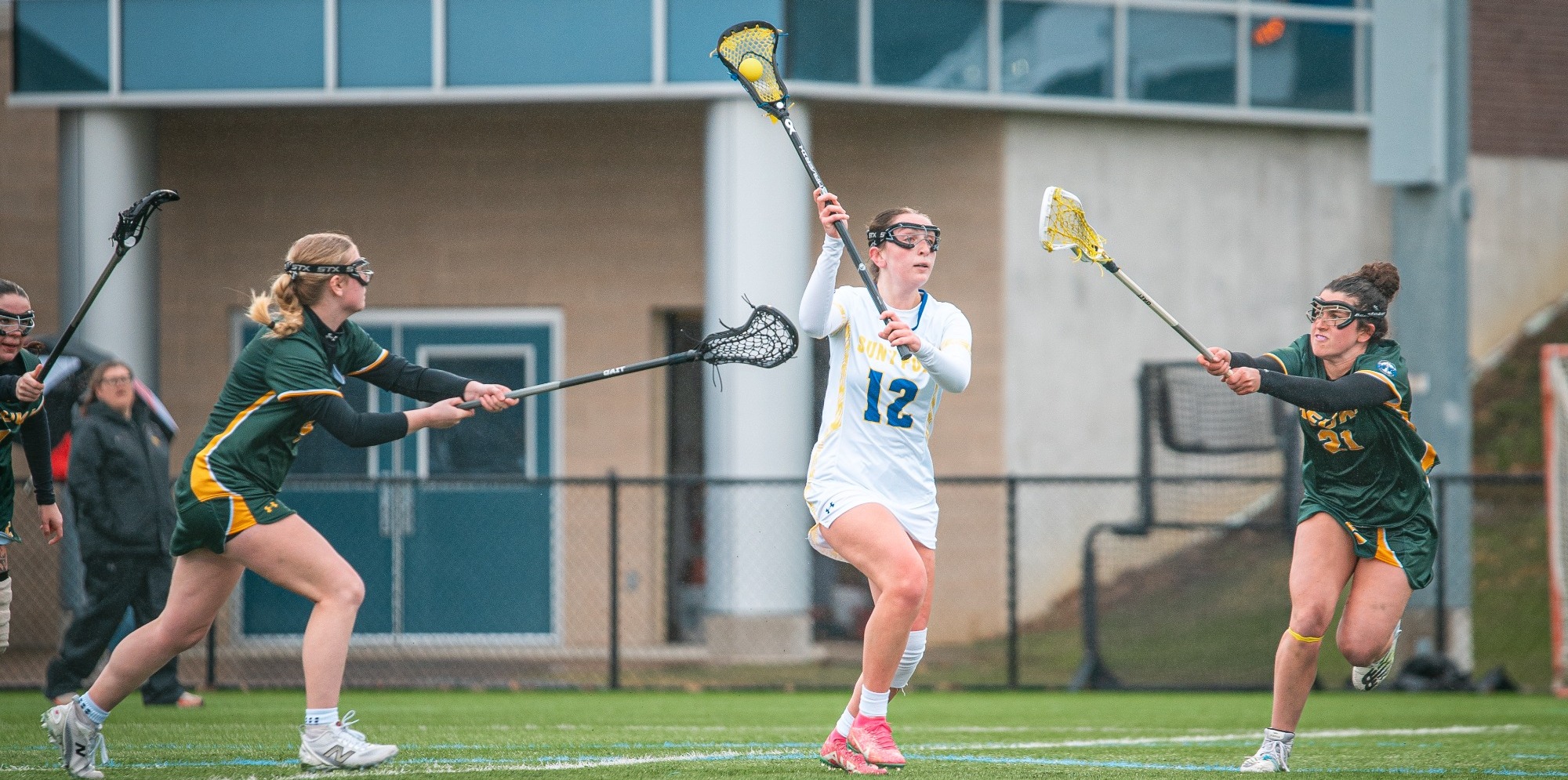 SUNY POLY women's lacrosse players splits two defenders as she makes an attempt to clear the ball