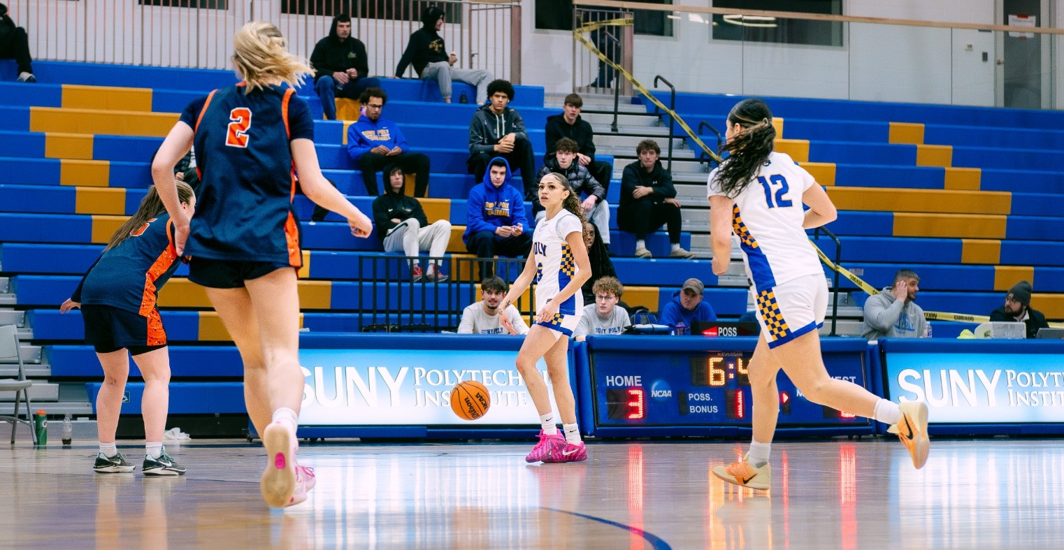 Women's basketball player dribbles ball up the court as rest of team gets prepared to run a play