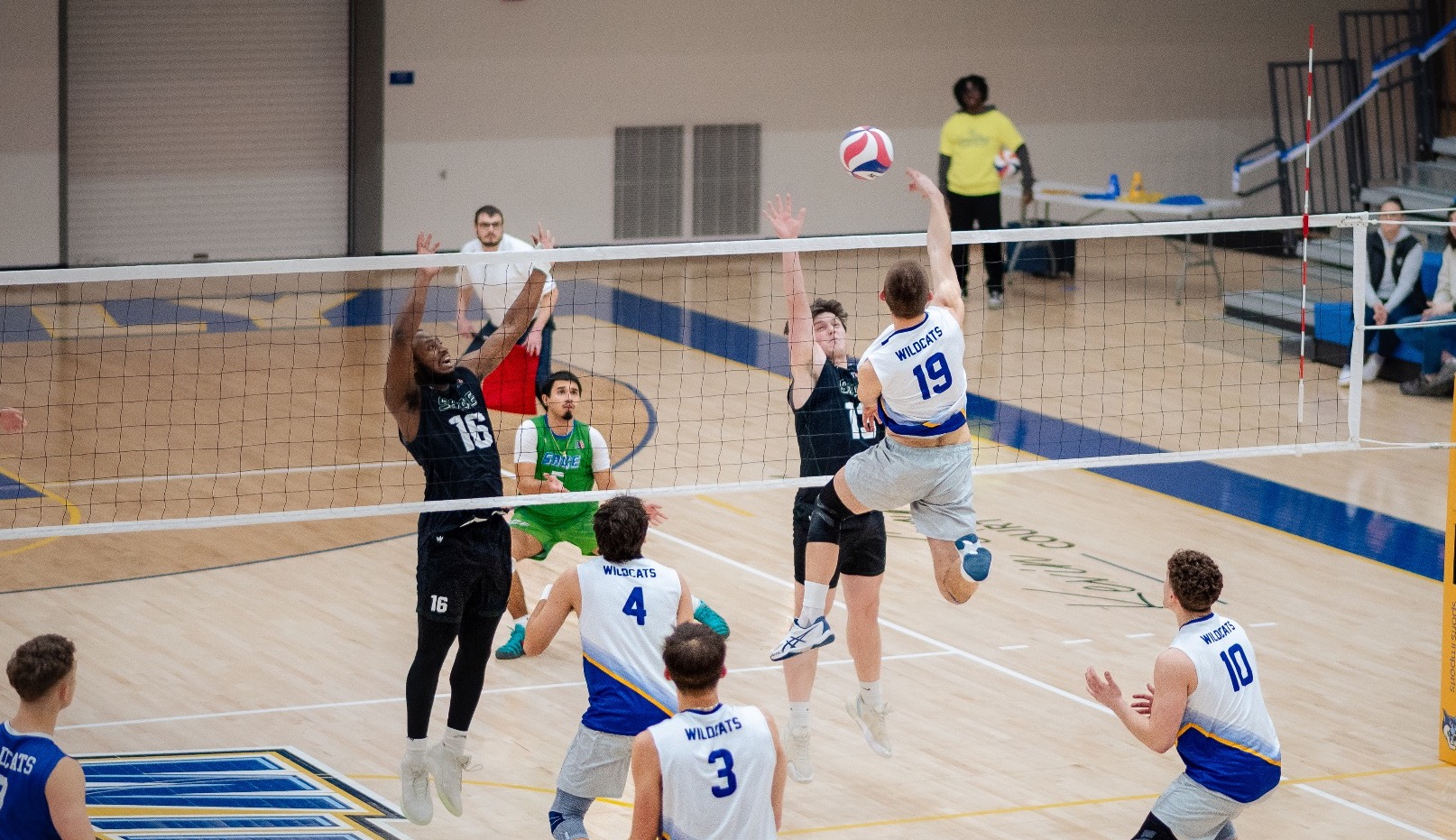 SUNY POLY men’s volleyball player goes up for the attack while teammates prepare to play defense 