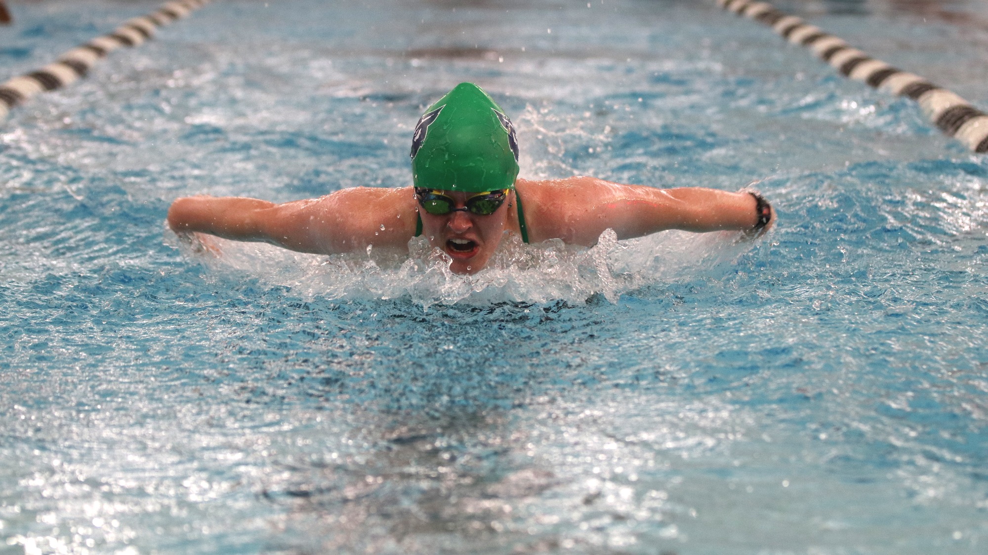 2023-2024 Women's Swimmer, Lucy Crayton swims the butterfly in the pool.