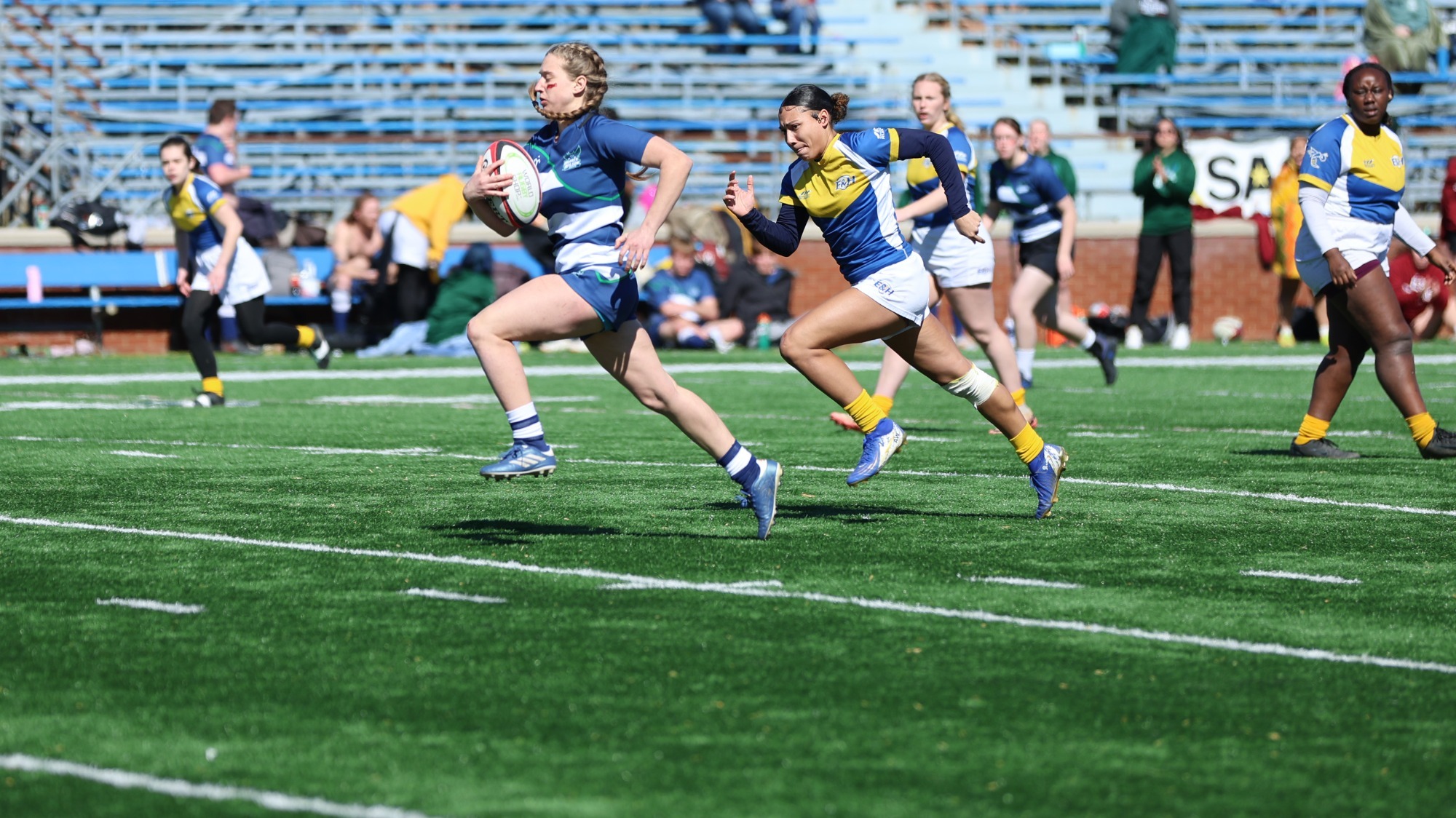 2025 Women's rugby player, Ella Knecht, runs down the middle of the field with the ball towards the try zone.